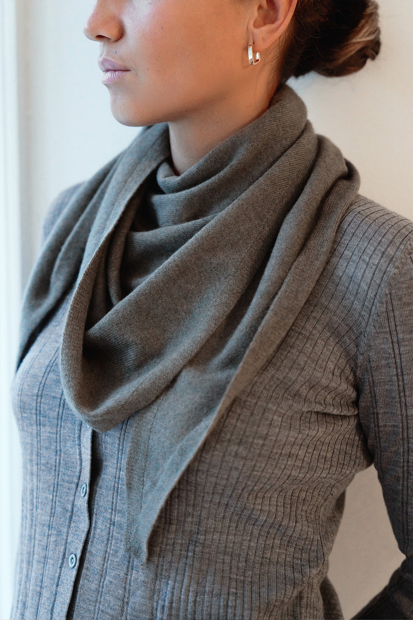Person wearing a gray scarf and gray sweater against a neutral background