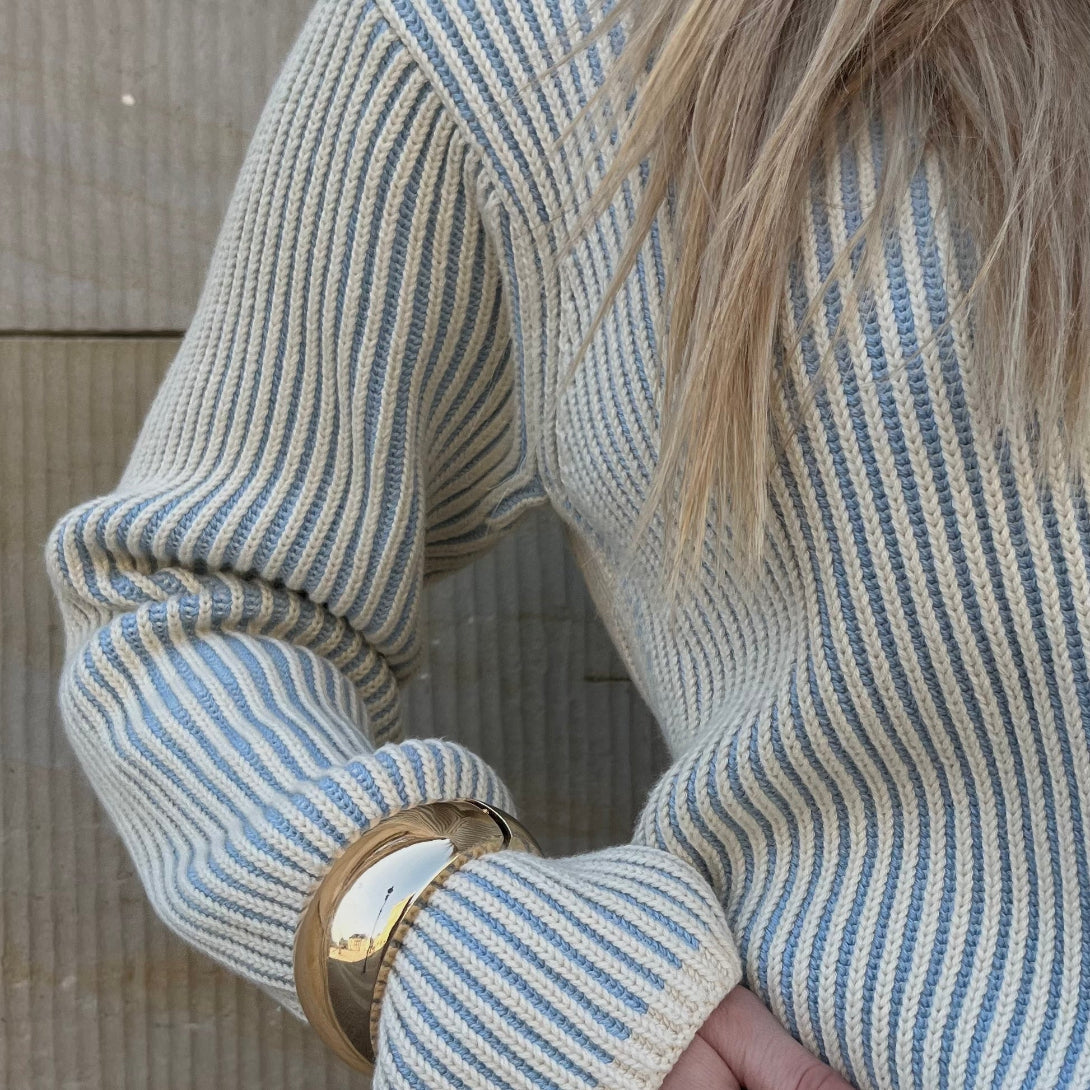 CYME-strikket sweater med lyseblå og cremefarvede striber. Sweateren er stylet med guld accessories.