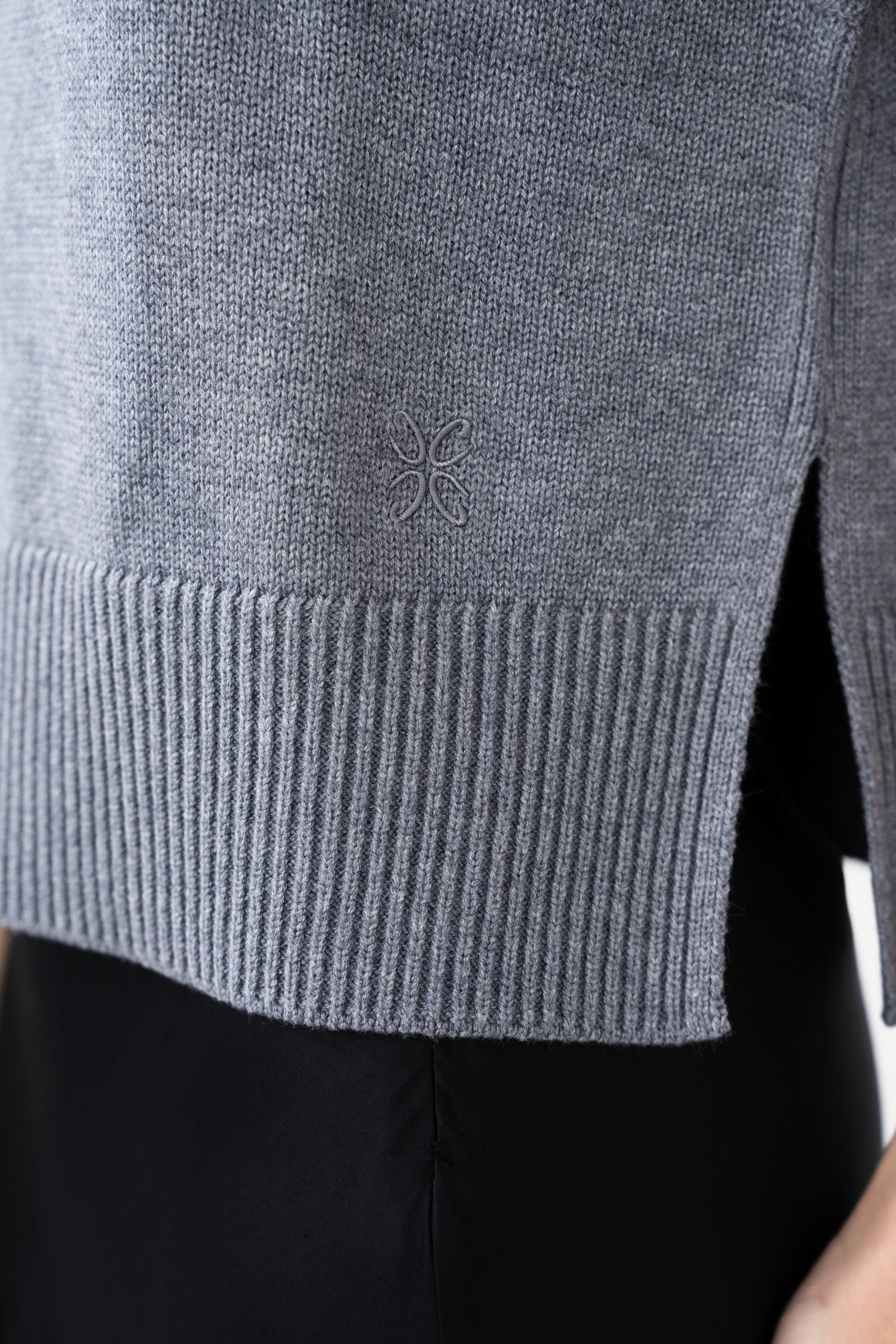 Close up of a grey knitted vest with a CYME monogram.