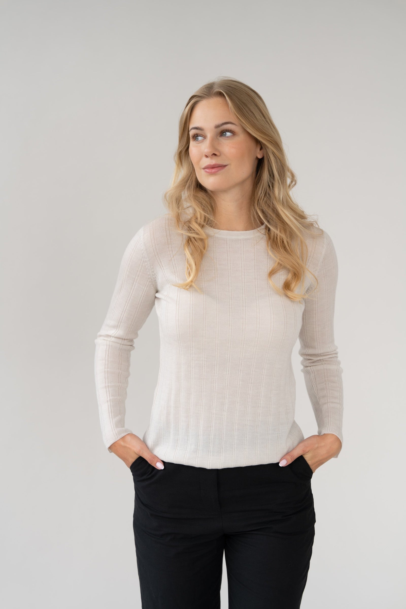 Woman wearing a white long-sleeve knit rib top and black pants against a plain background