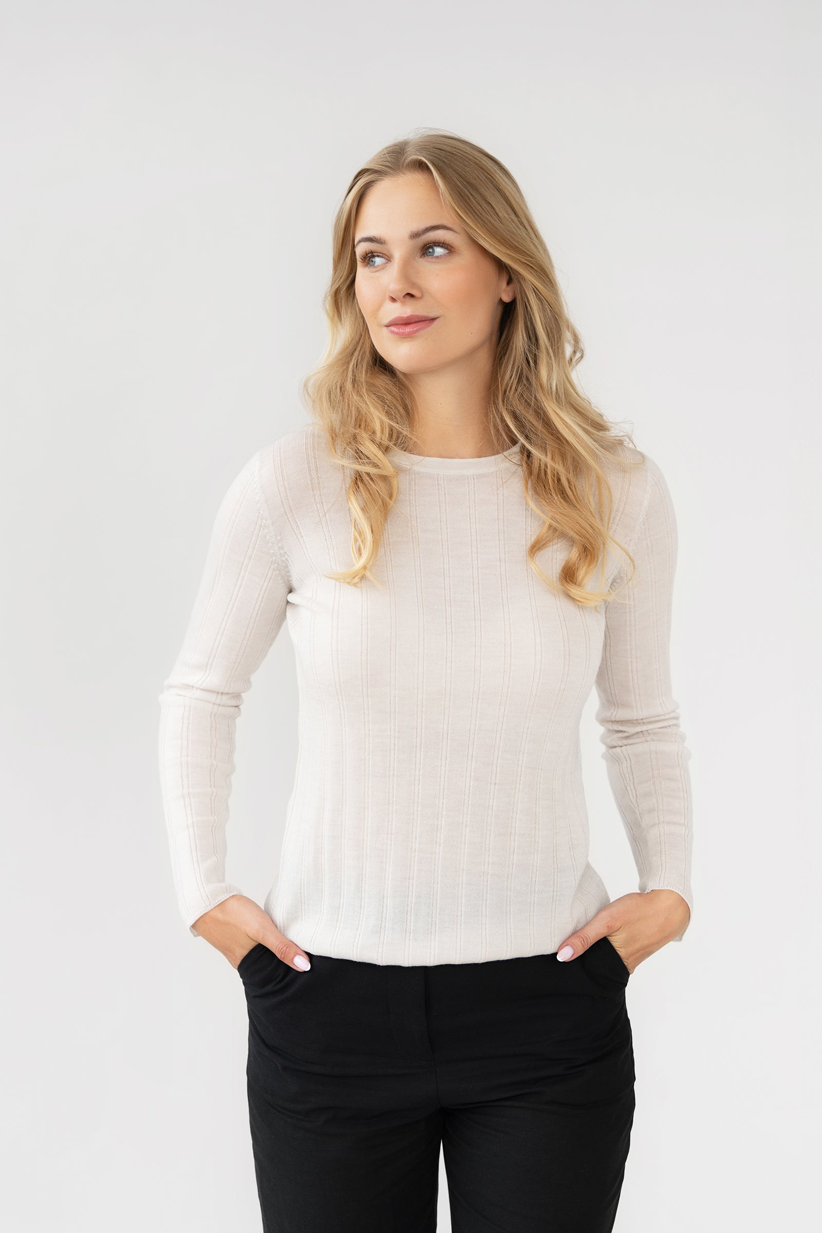 Woman wearing a white long-sleeve knit rib top and black pants against a plain background