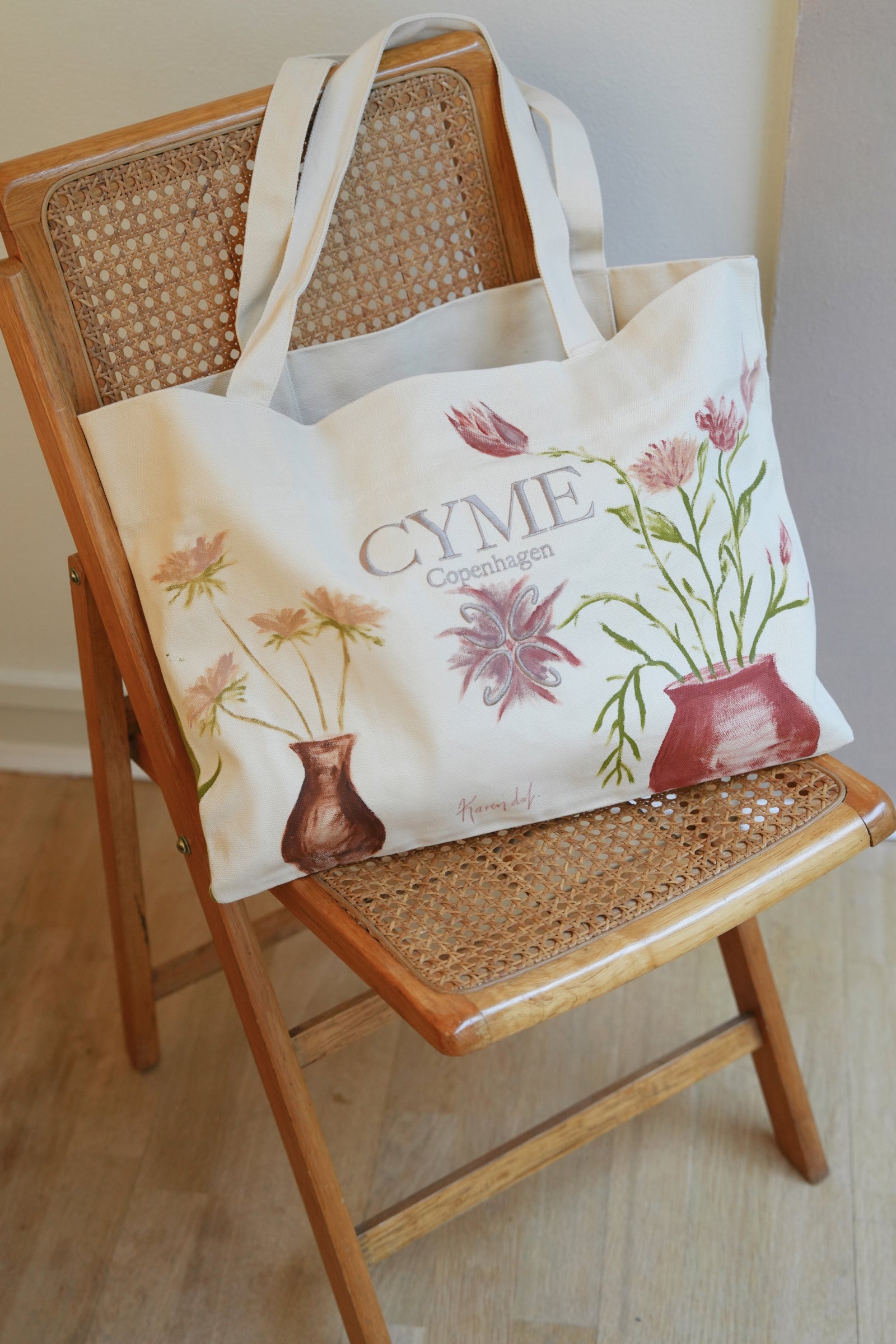 Tote bag with floral design and 'CYME' branding on a wooden chair.