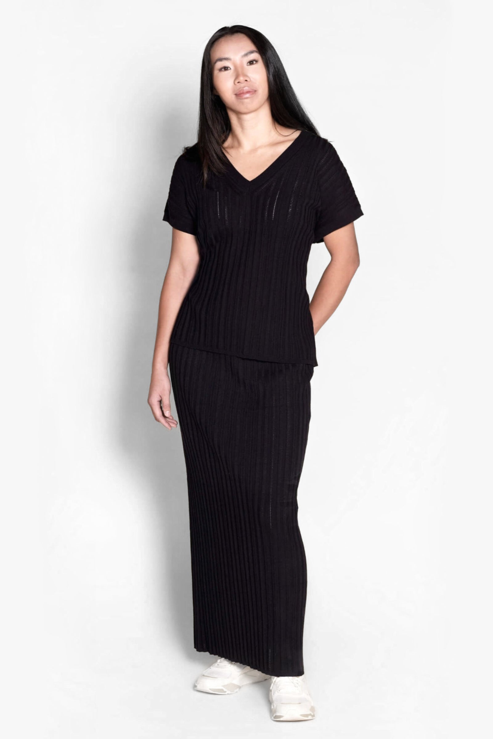 Model elegantly dons a Cyme Copenhagen all-black ribbed knit ensemble, featuring a V-neck top and matching skirt, a chic example of the brand's sustainable fashion offerings in women's clothing from a top Danish designer.
