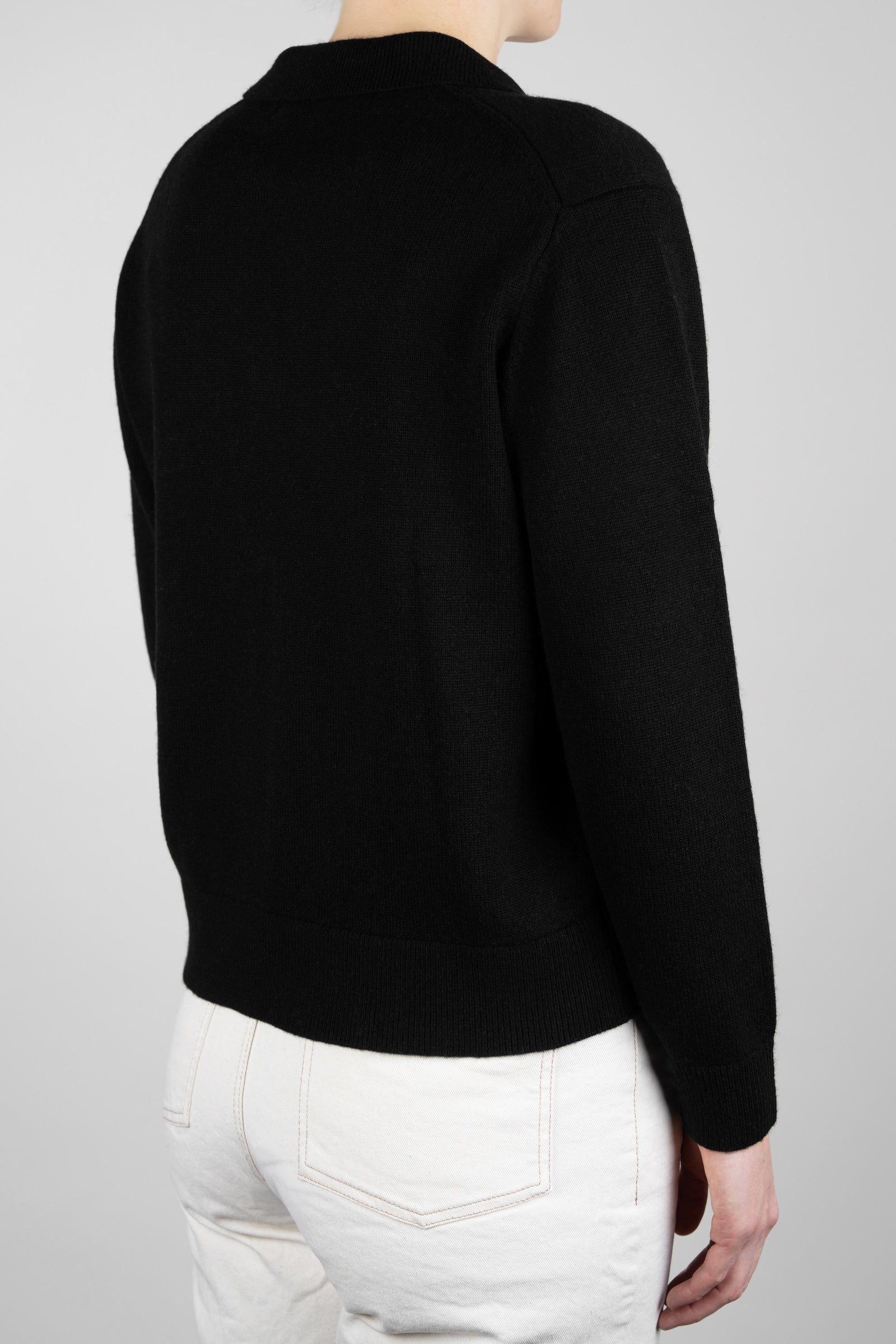 Person wearing a black sweater and white pants on a gray background