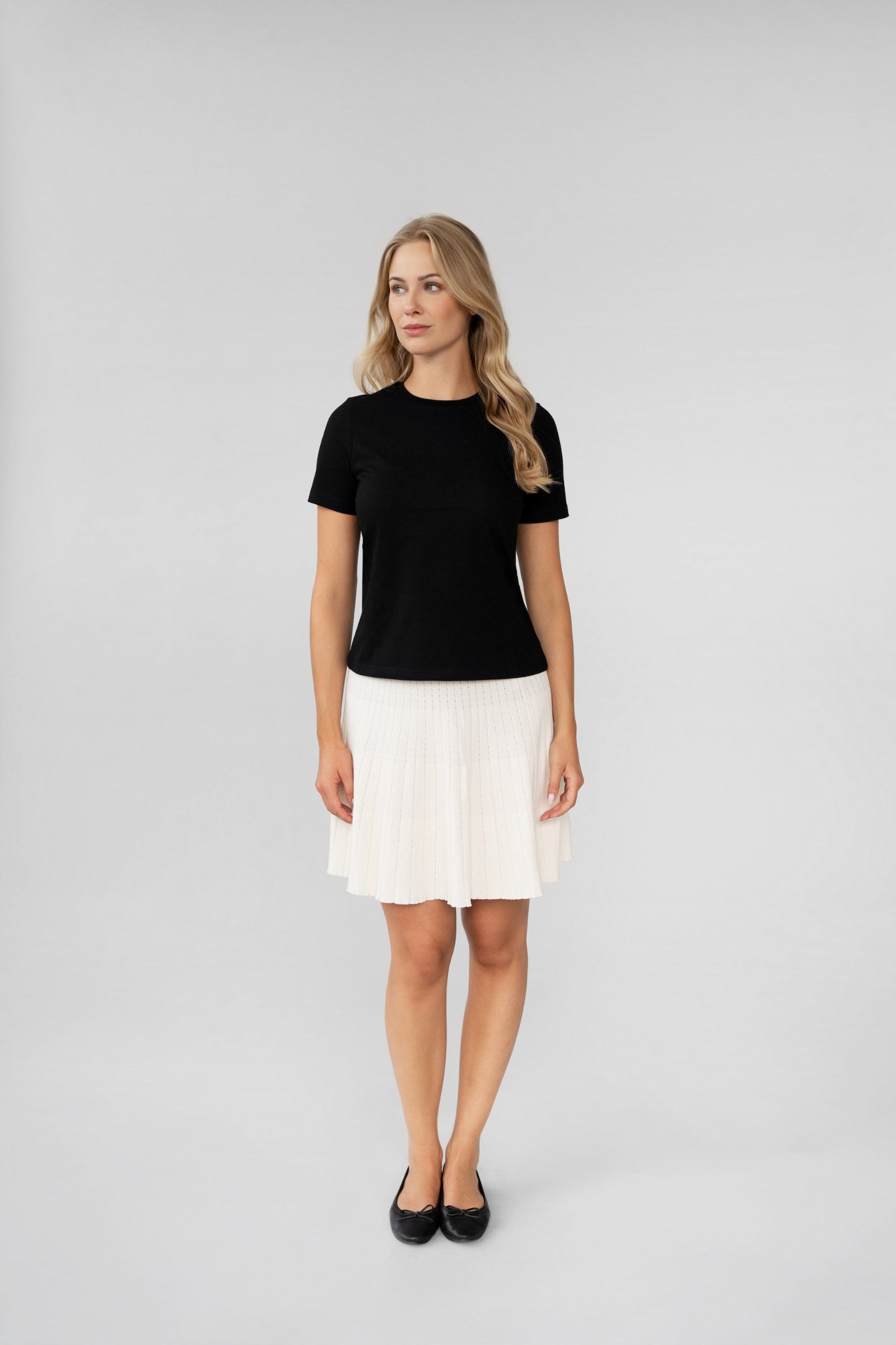 Woman wearing a black top and white skirt on a gray background