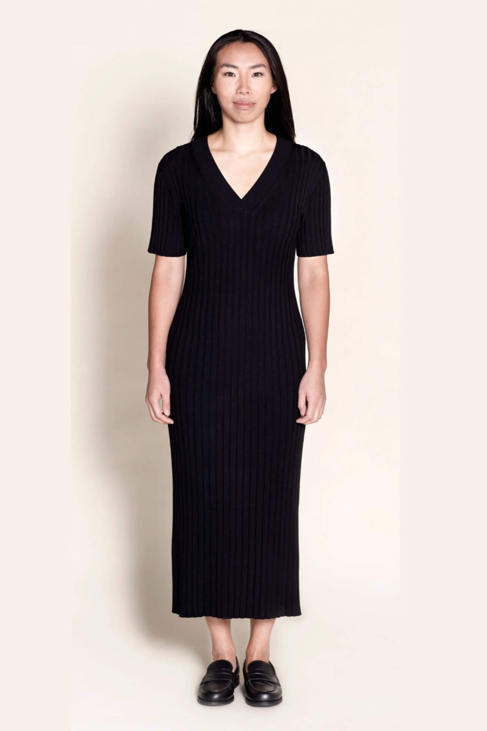 Model wears Cyme Copenhagen's classic black ribbed knit midi dress, featuring a flattering V-neck and short sleeves, a testament to sustainable, versatile women's fashion by a Danish designer.
