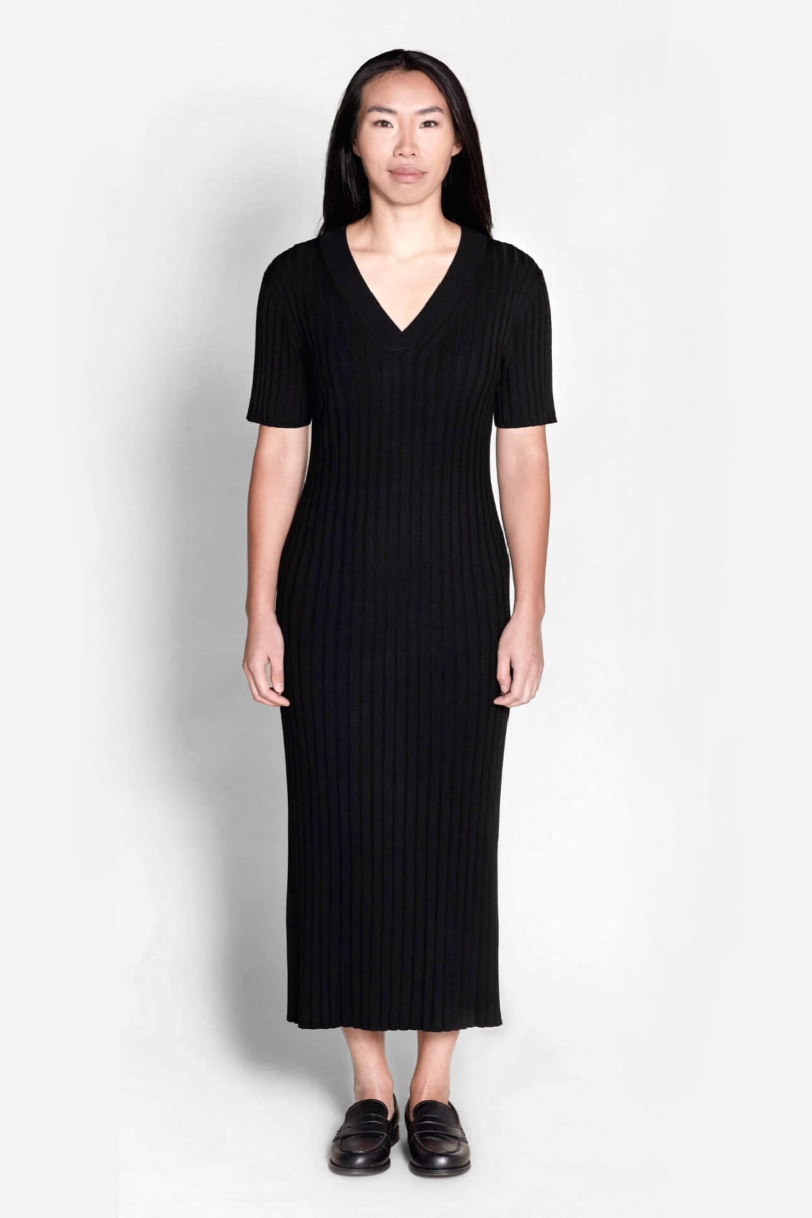 Model wears Cyme Copenhagen's classic black ribbed knit midi dress, featuring a flattering V-neck and short sleeves, a testament to sustainable, versatile women's fashion by a Danish designer.
