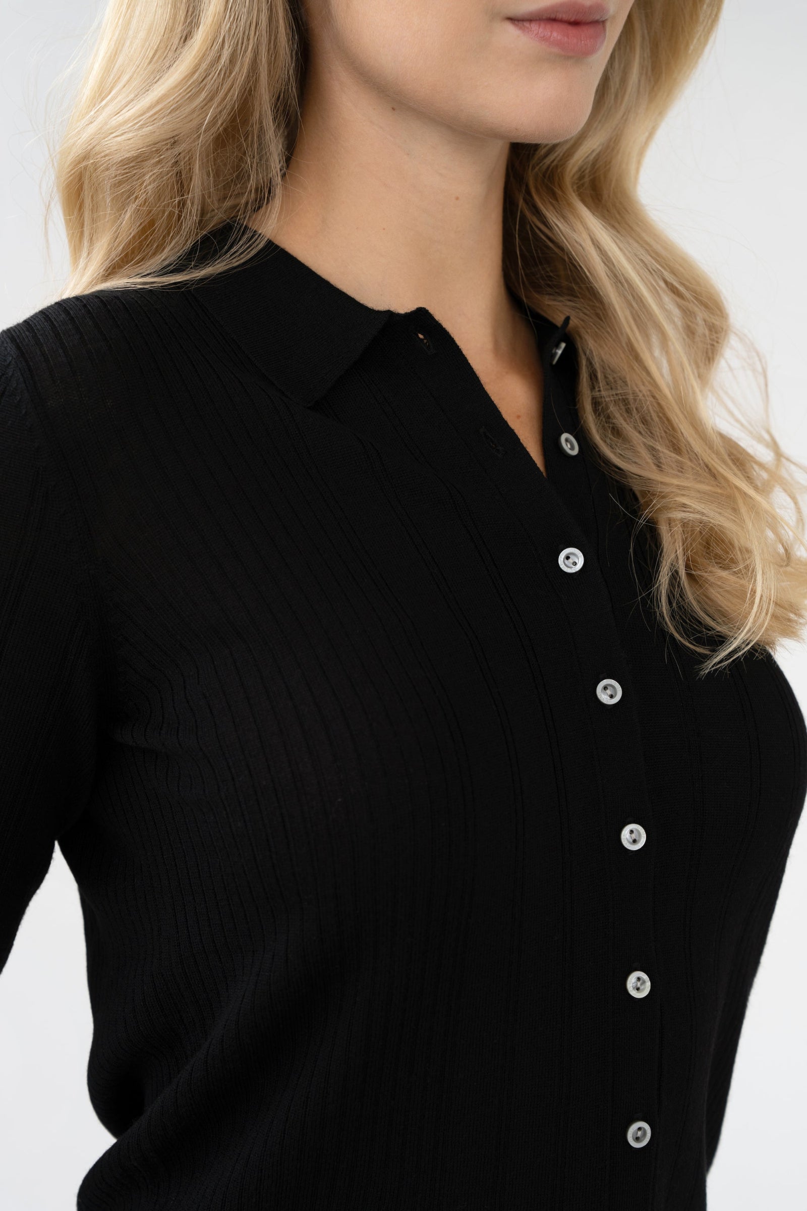 Close-up of collar and branded buttons on ribbed knit collared cardigan, black, studio.