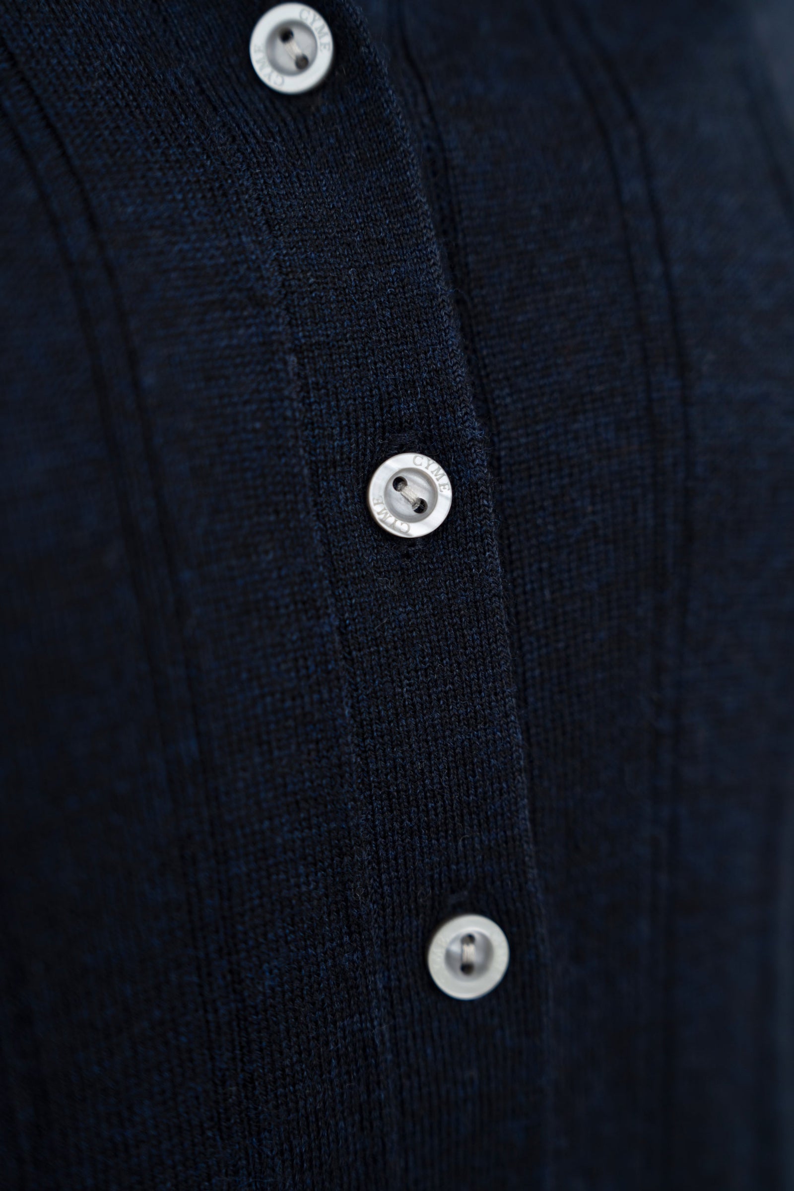 Close-up detail of branded buttons on ribbed knit collared cardigan, navy, studio.