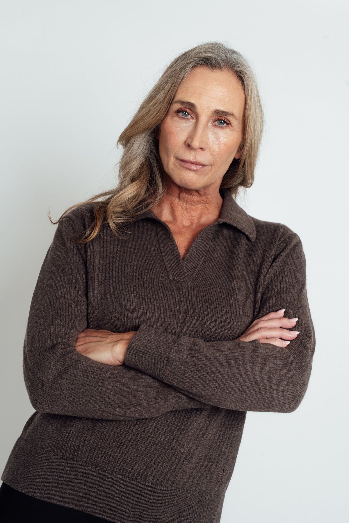 Close-up of the dark brown Cashmere-Merino Polo Jumper's open collar and ribbed cuff, with arms folded.