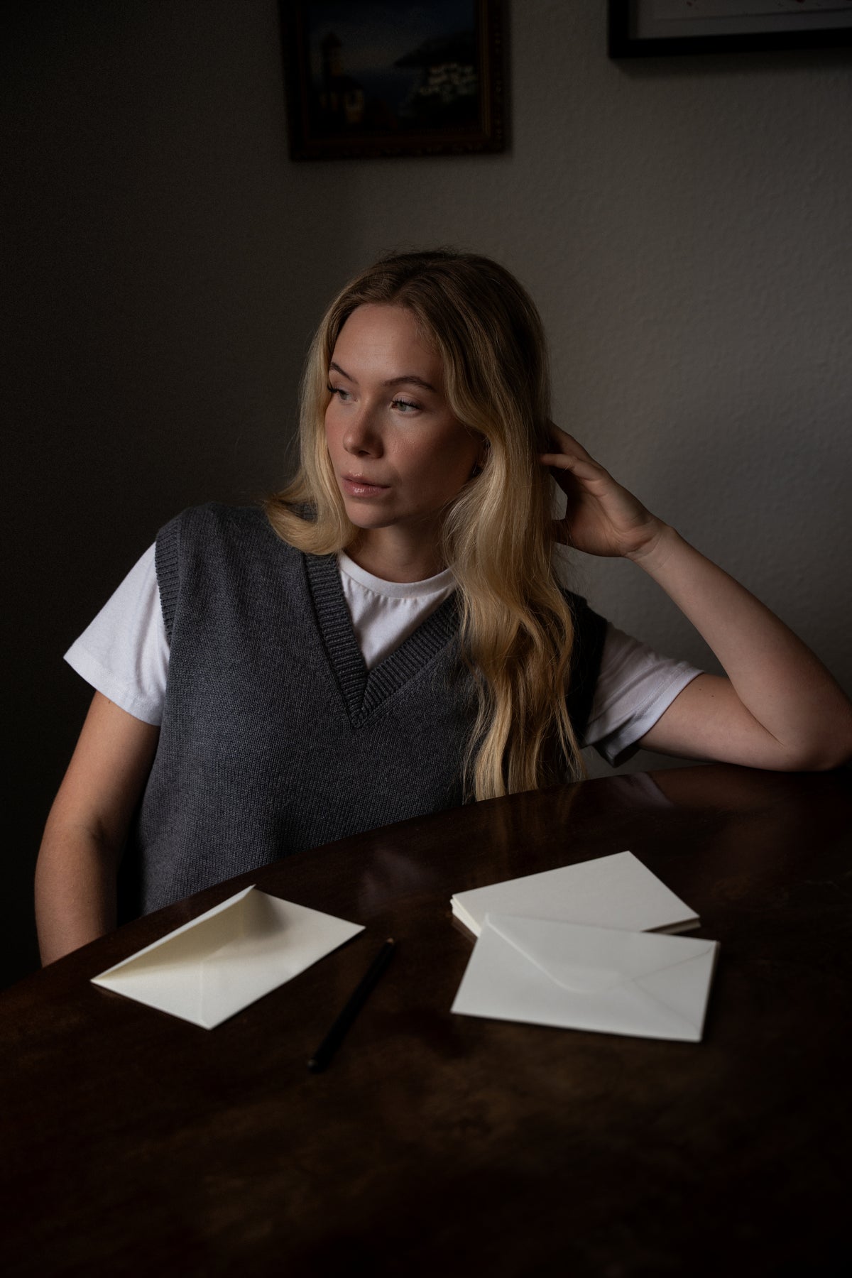 A woman seated at a wooden desk wearing the grey CYME Merino V-Neck Vest over a white T-shirt.