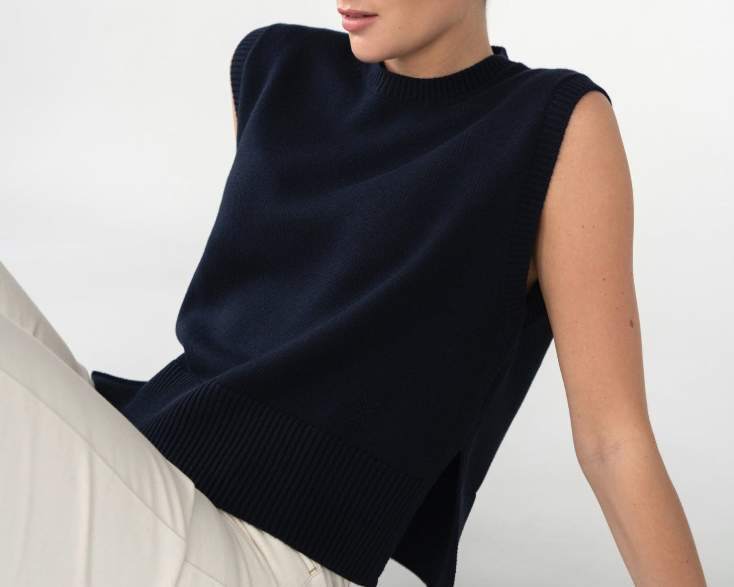 Woman wearing a navy blue sleeveless top sitting on a white surface with a white background