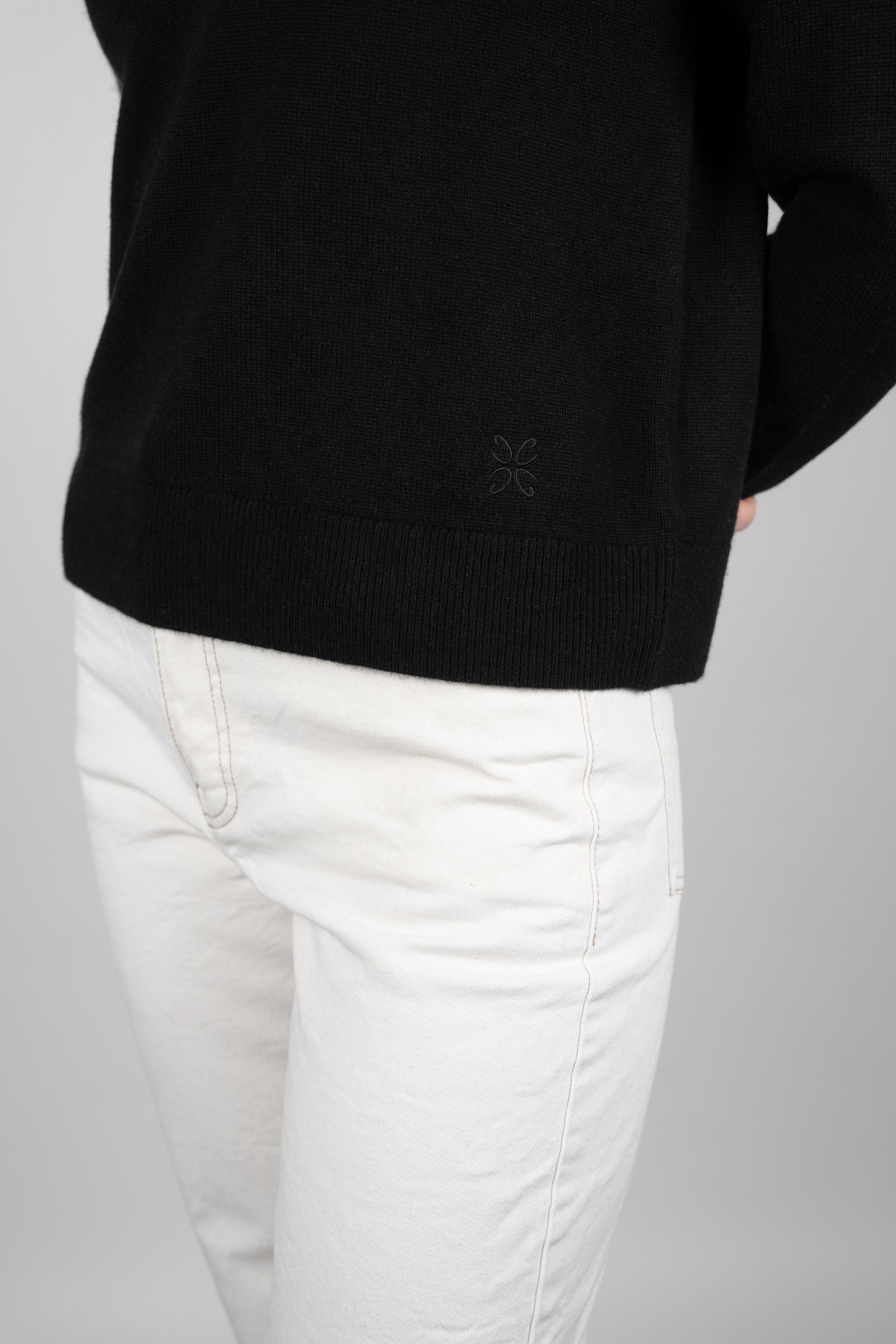 Person wearing a black sweater and white pants on a gray background
