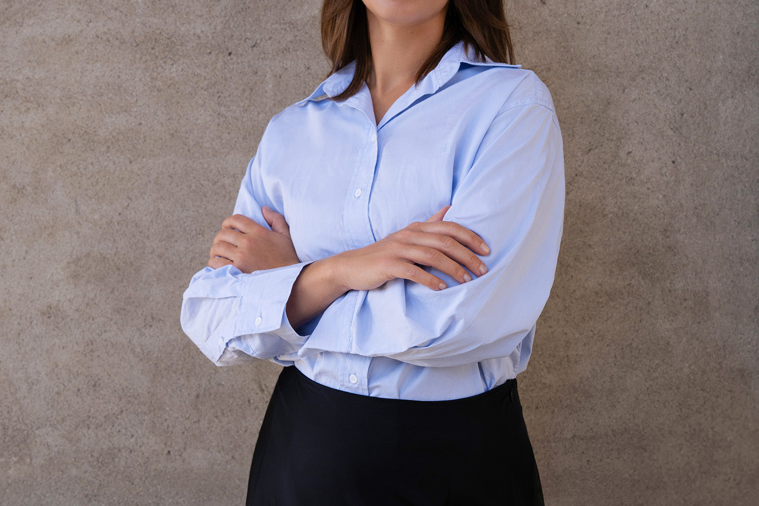 Person wearing a light blue shirt with rolled-up sleeves against a neutral background