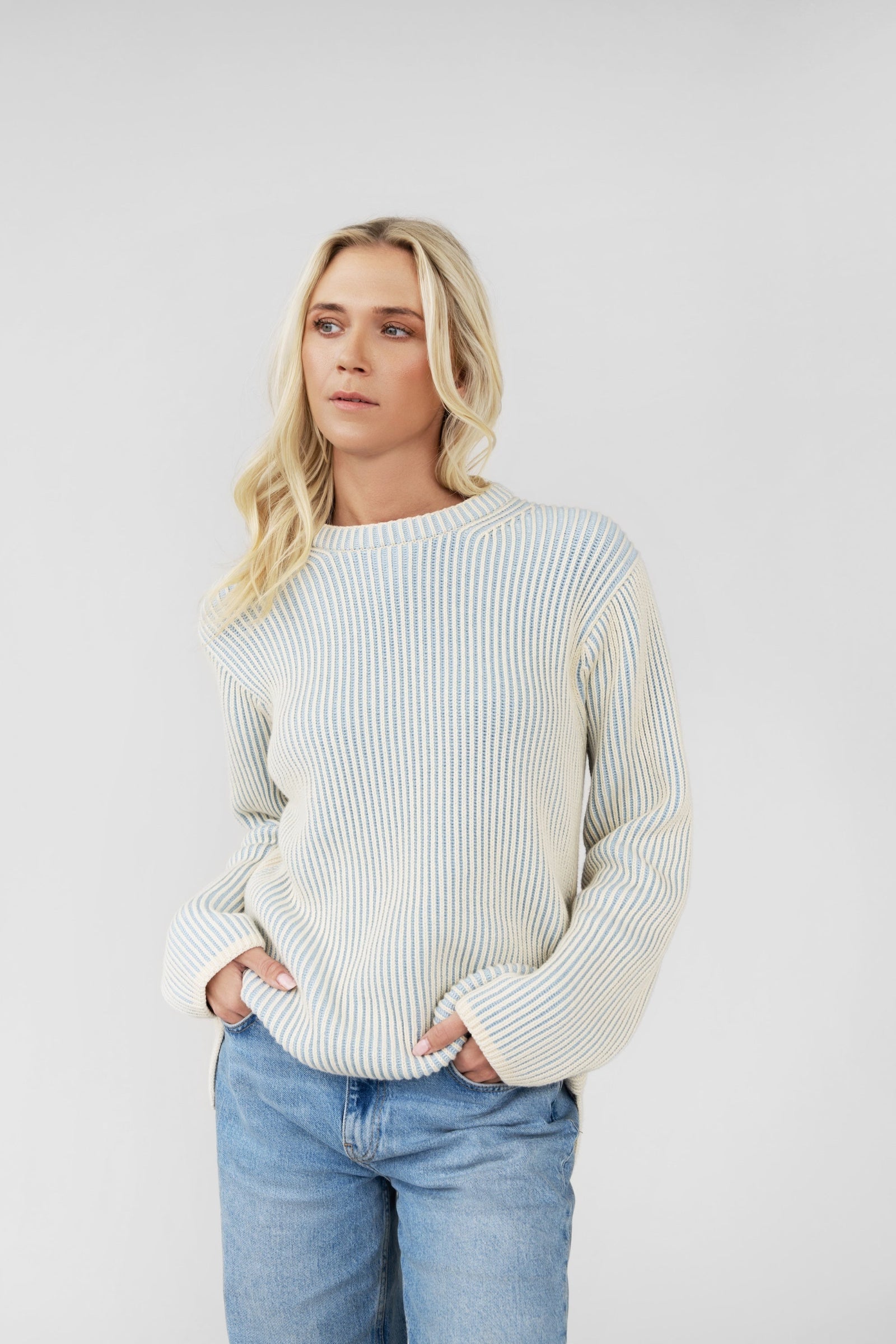 Woman wearing a white ribbed sweater and light blue jeans against a plain background