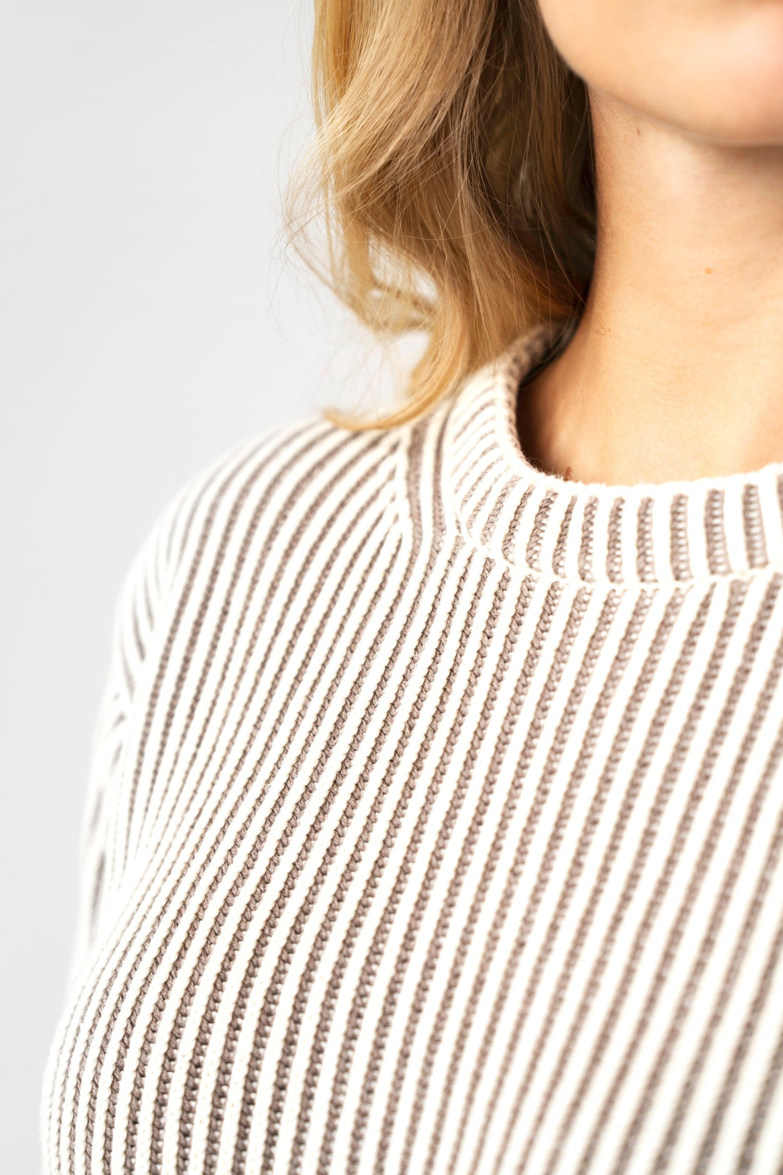 Close-up of a person wearing a ribbed knit sweater against a plain background