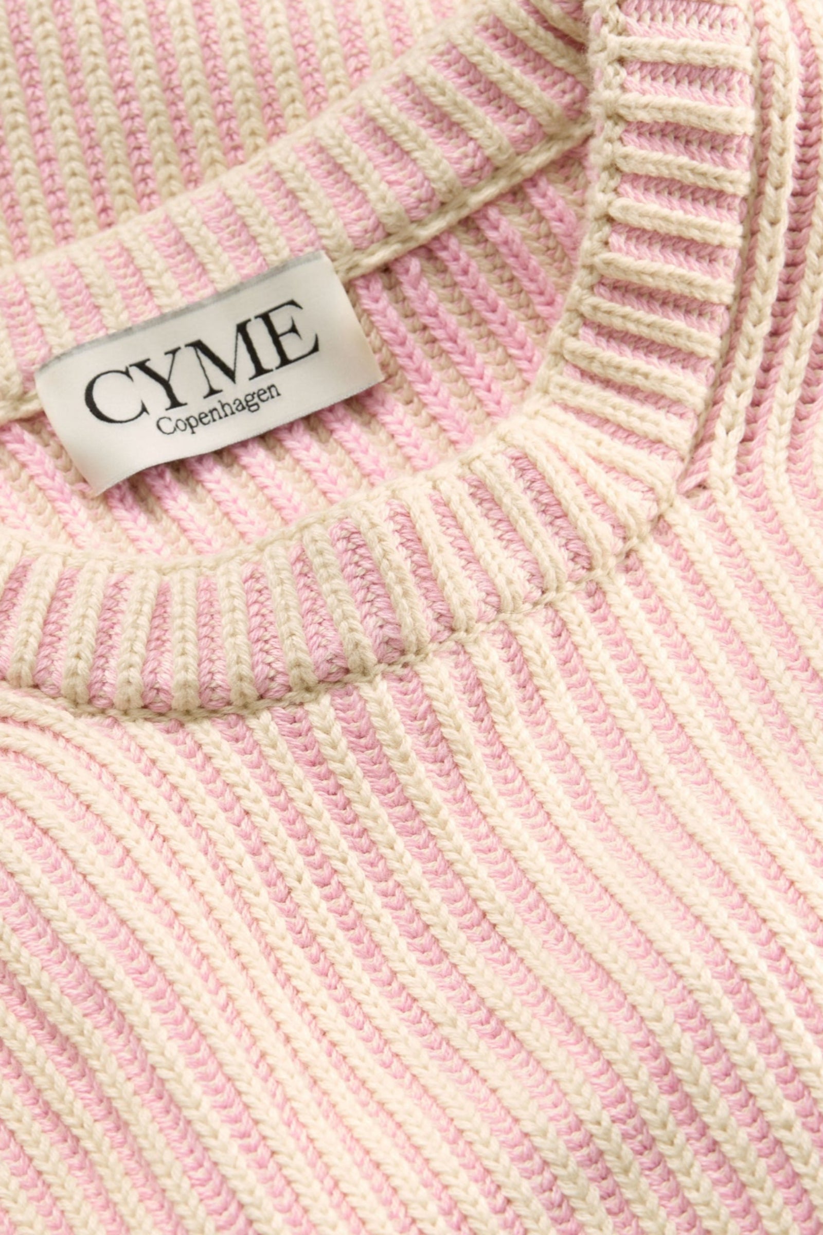 A close-up of the neckline and ribbed texture of a cream and light pink sweater.