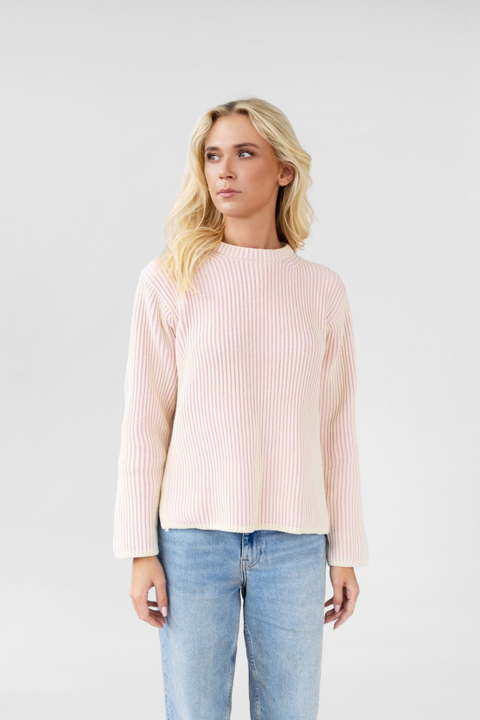 Woman wearing a light pink ribbed sweater and blue jeans on a white background