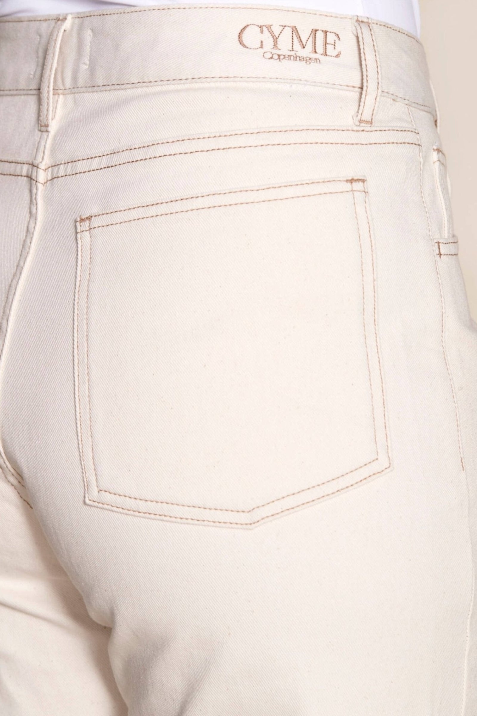 Detail of Cyme Copenhagen's cream denim pants, focusing on the back pocket with branded tag, emphasizing the brand's quality craftsmanship and ethical fashion standards in Denmark's clothing shops.
