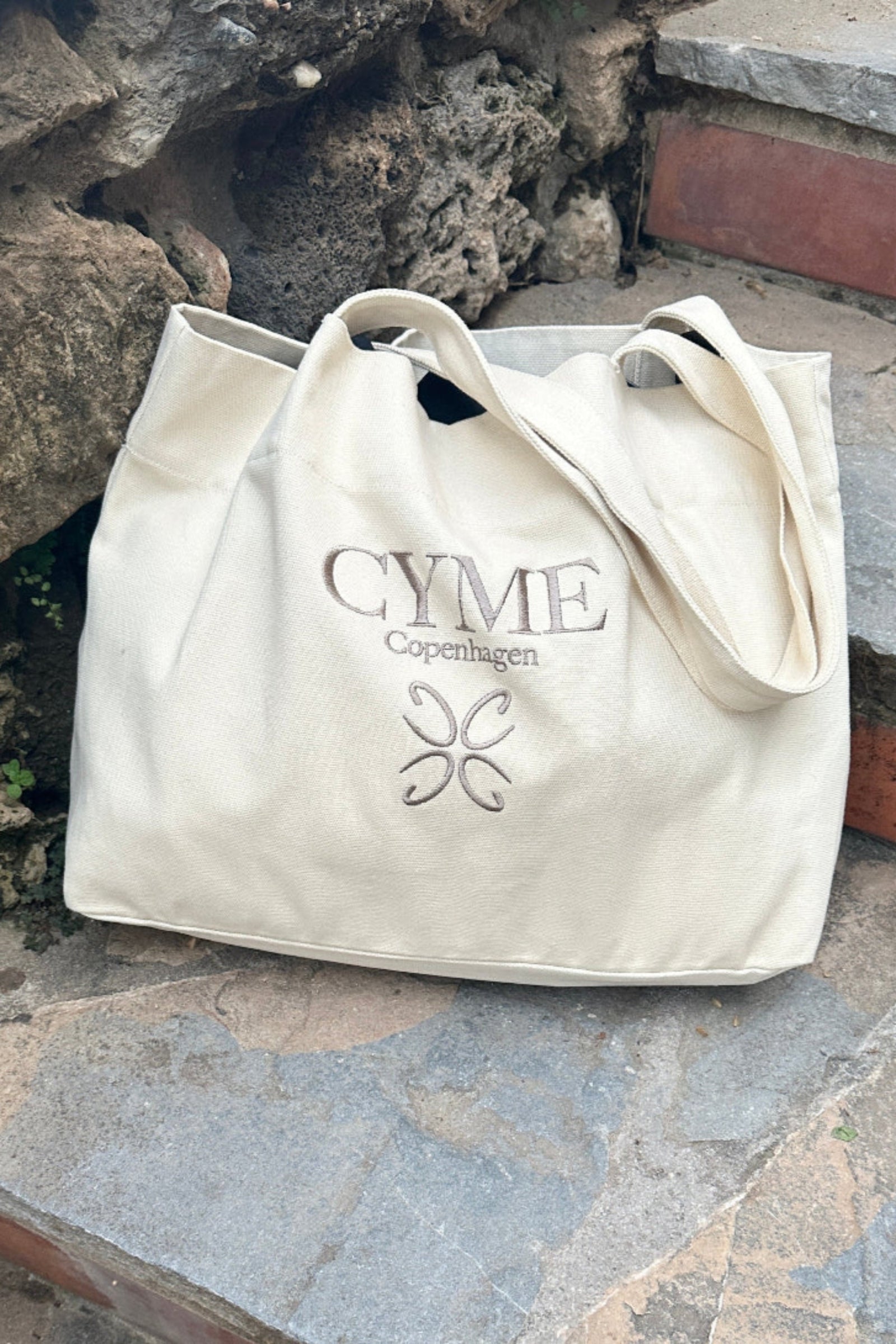 A cream colored CYME Copenhagen tote bag placed on stairs.