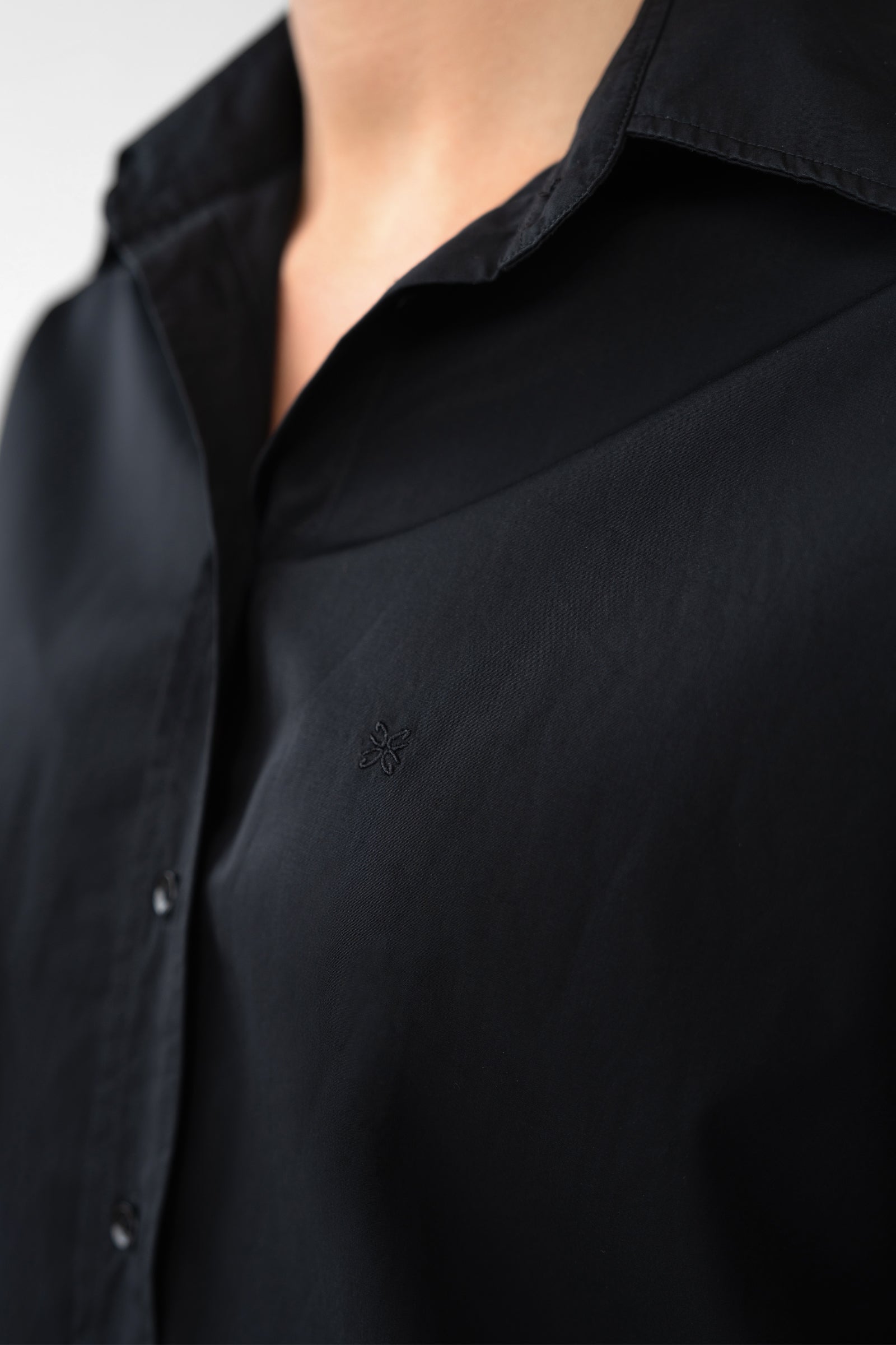 Close-up of a black shirt with a brand logo on a light gray background
