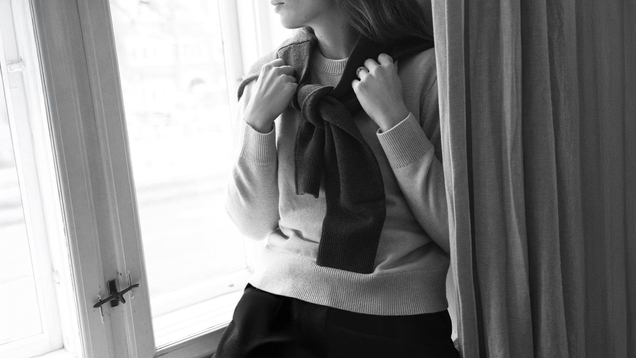 Black and whirte photo of a woman wearing a crewneck jumper with a brown polo jumper draped over her shoulders.