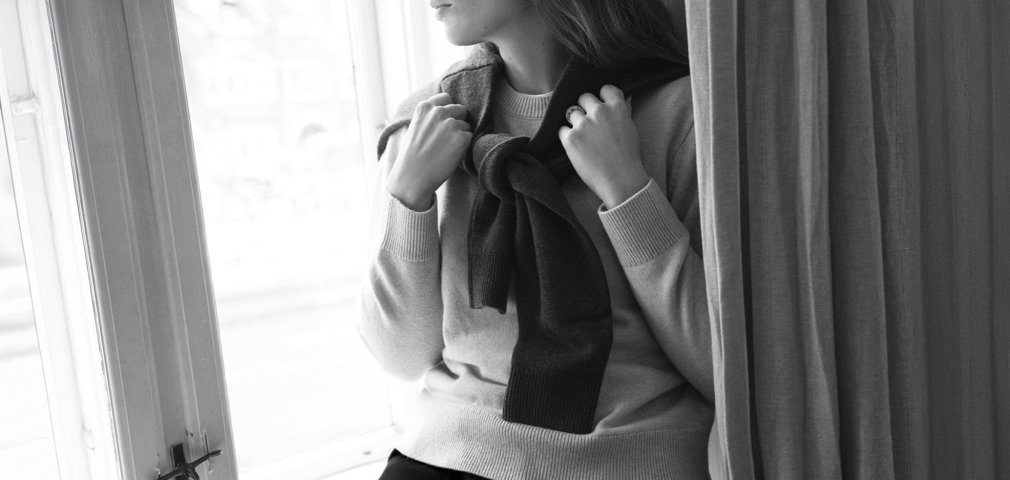 Black and whirte photo of a woman wearing a crewneck jumper with a brown polo jumper draped over her shoulders.