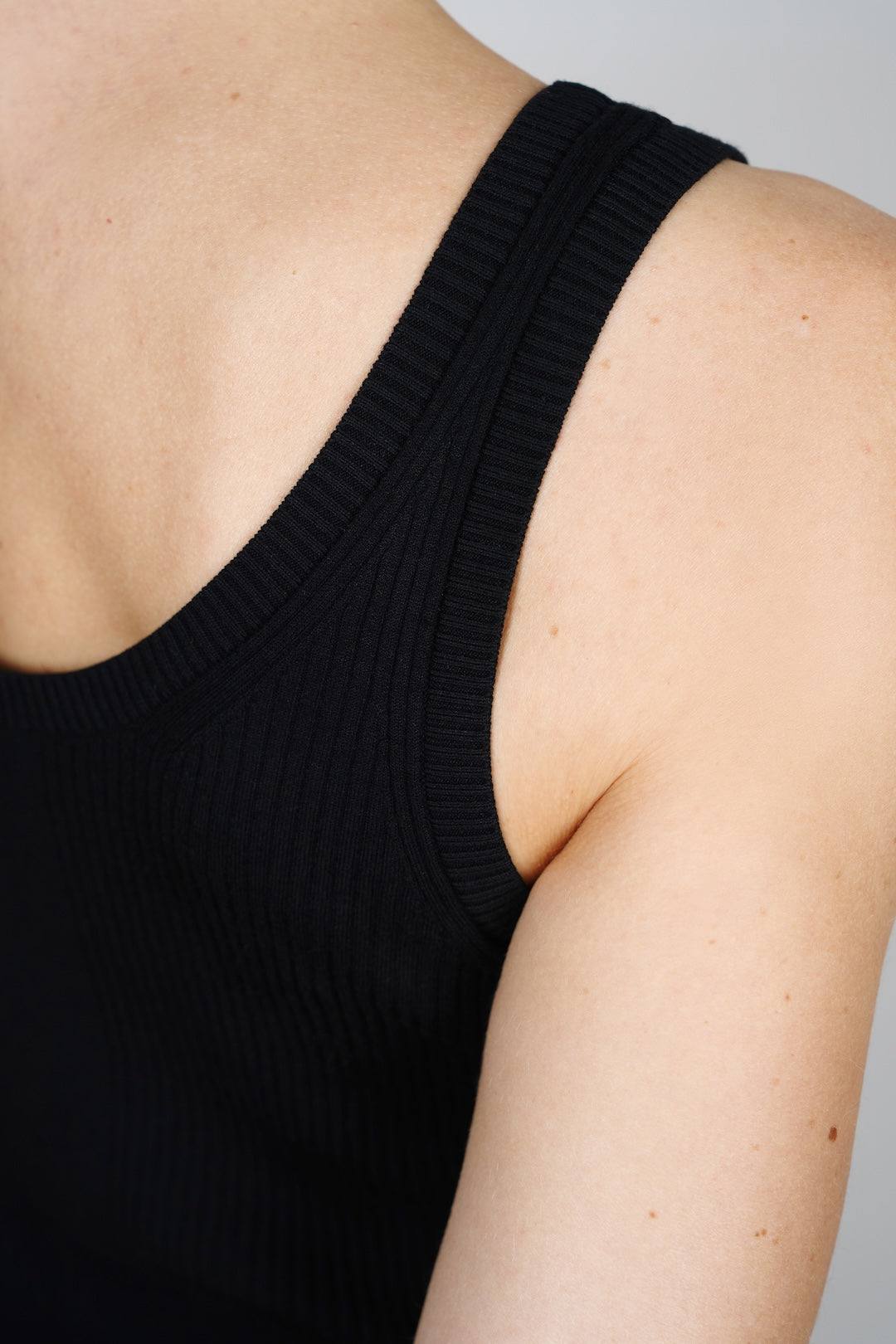 Detail view of the CYME Essential Top in black, focused on the ribbed shoulder strap and clean armhole. Made from a soft, stretchy knit for everyday ease.