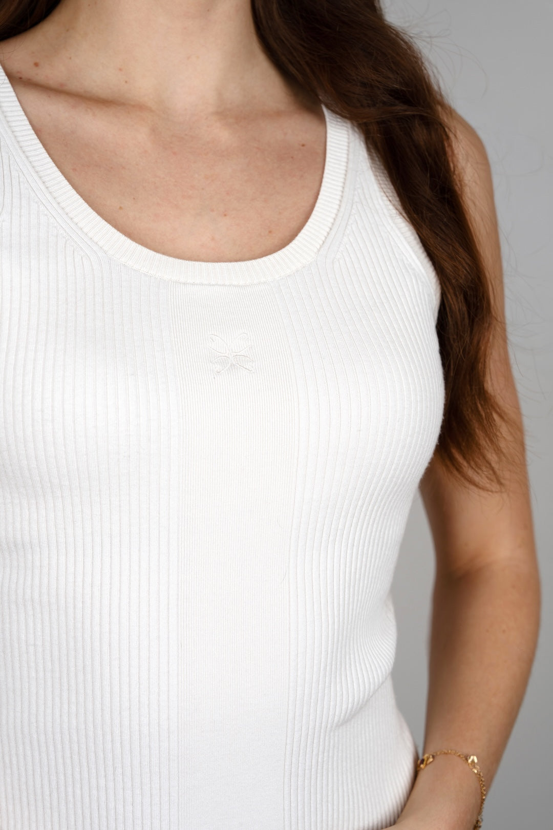 Detail view of the CYME Essential Top in ivory, focused on the scoop neckline and subtle tonal embroidered CYME logo. Its seamless ribbed knit feels soft against the skin.