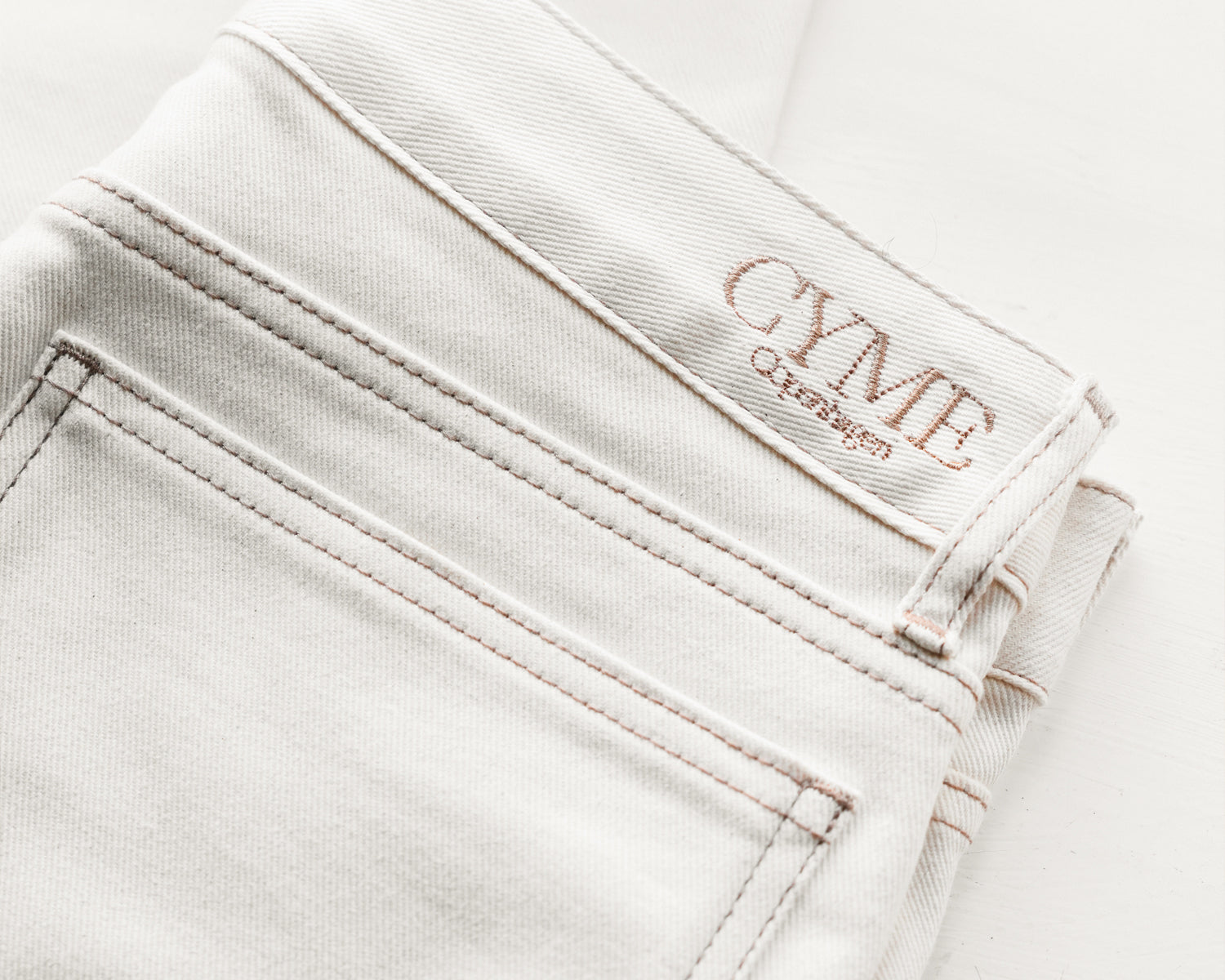 White jeans with 'CYME Copenhagen' branding on a beige background