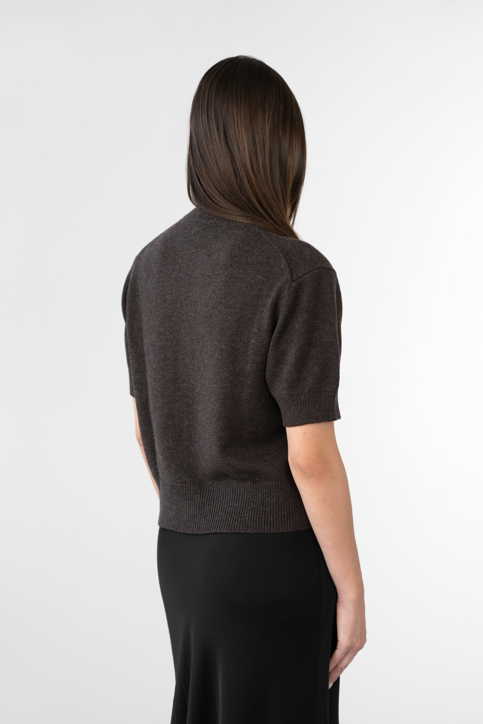 On-model back view of women's short-sleeve knit top, ribbed hem and cuffs, dark brown, studio.
