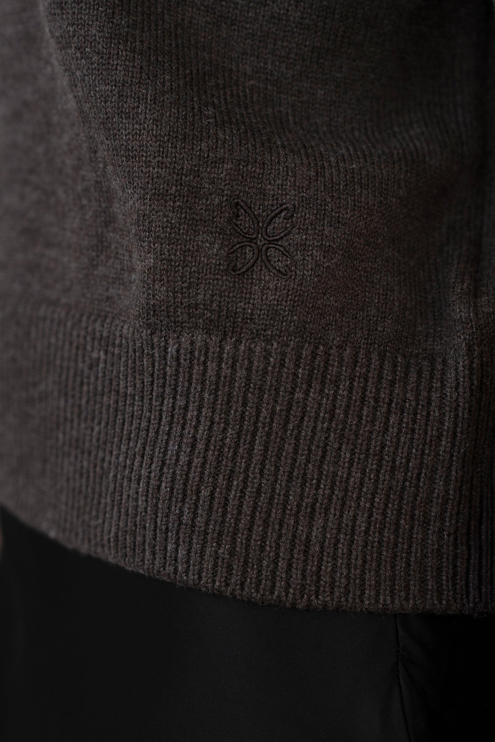 Close-up of ribbed hem with tone-on-tone embroidered logo on women's short-sleeve knit top, dark brown, studio.