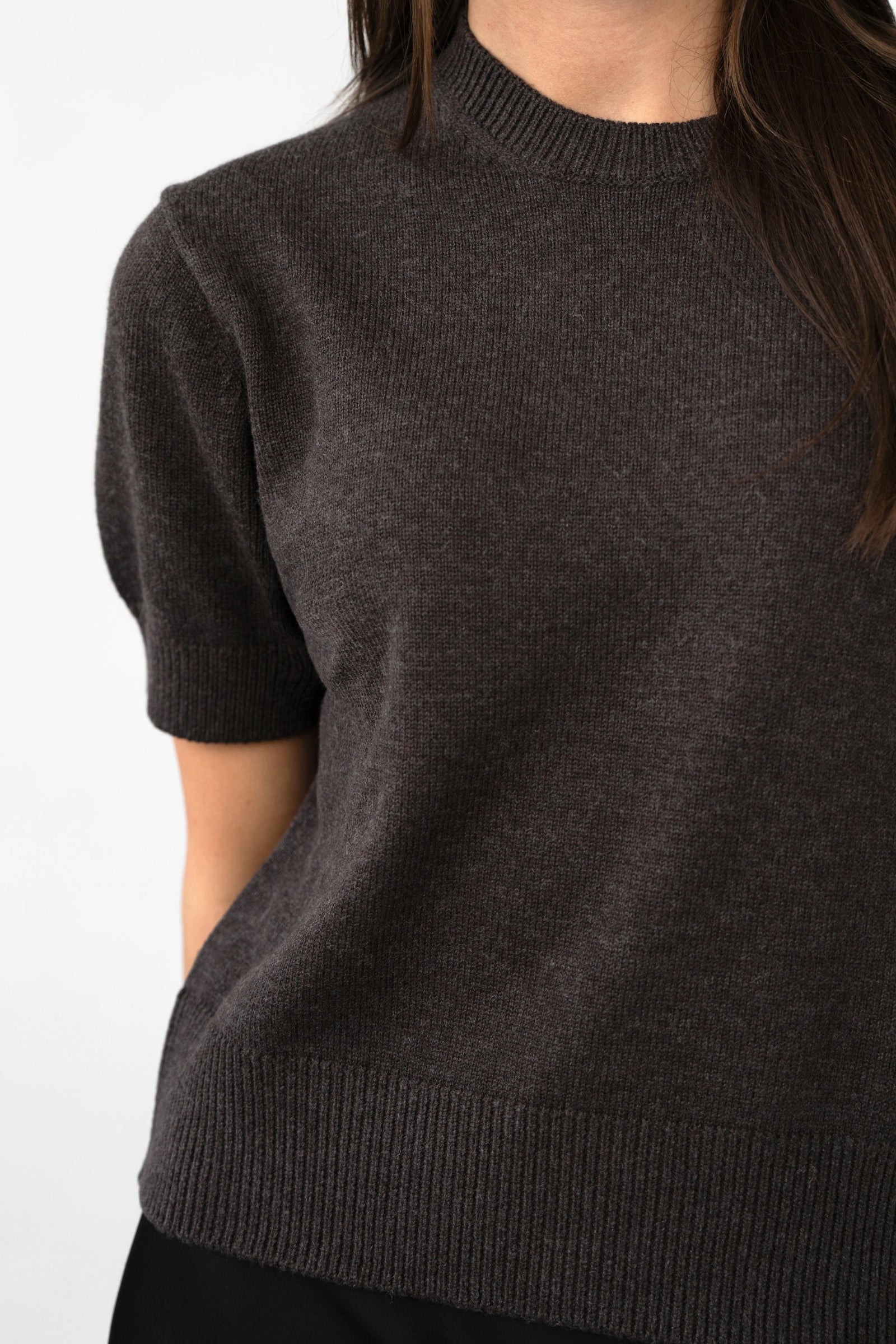 Close-up on-model detail of women's short-sleeve knit top, ribbed crew neck and hem, dark brown, studio shot.