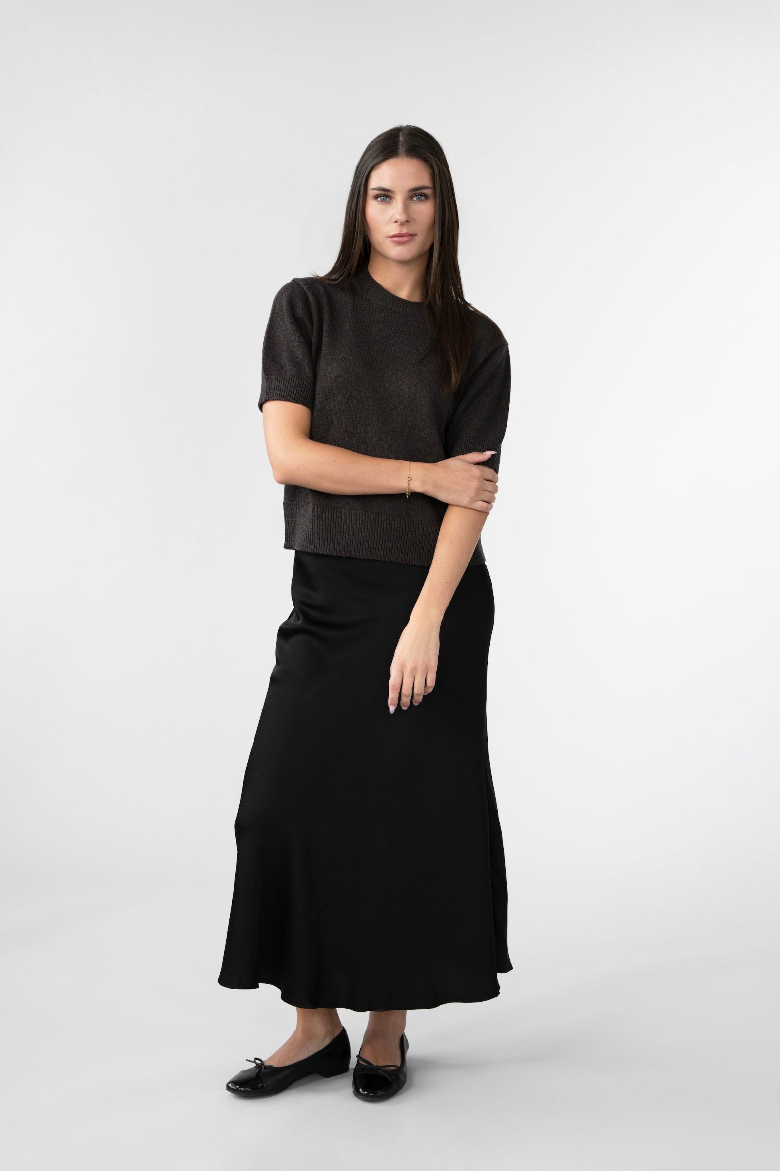 On-model full-length view of women's short-sleeve knit top, crew neck, dark brown, styled with black midi skirt.