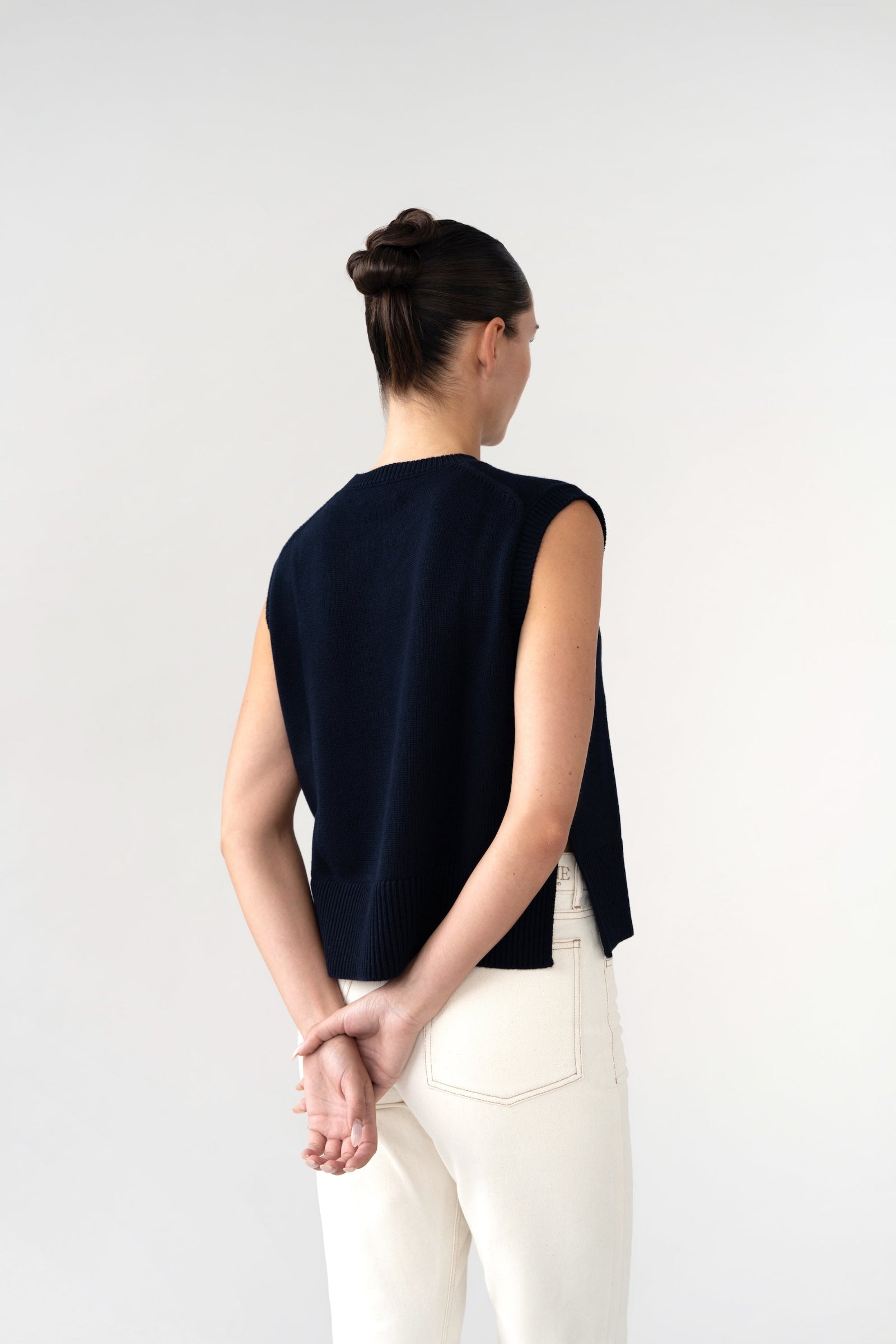 On-model back view of women's sleeveless knitted vest, navy, wide rib hem, studio.