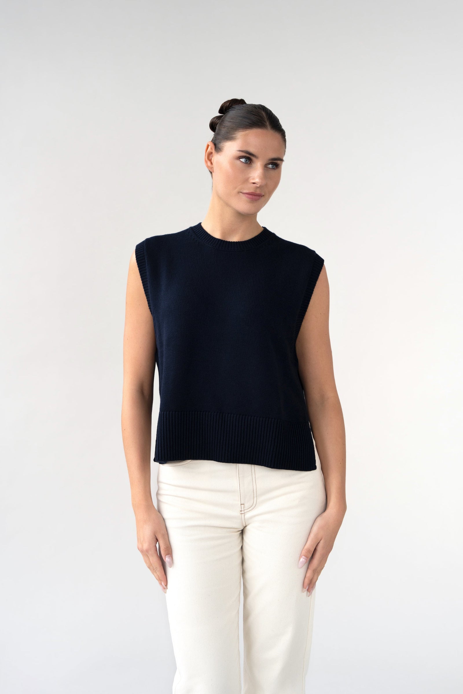 On-model front view of women's sleeveless knitted vest, navy, crew neck, styled with light jeans.