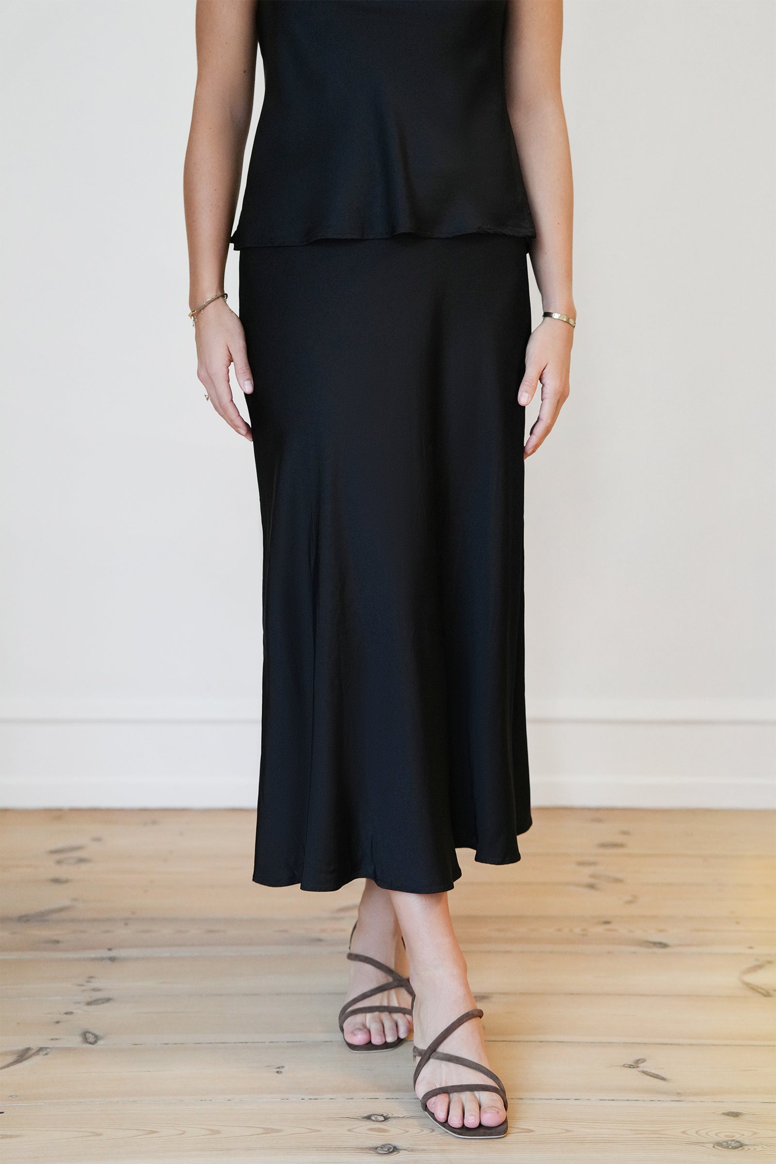 Front view of the CYME Satin Skirt in black. A high-waisted, ankle-length skirt with a fluid drape and subtle flare—made from elegant satin for refined movement and shine.