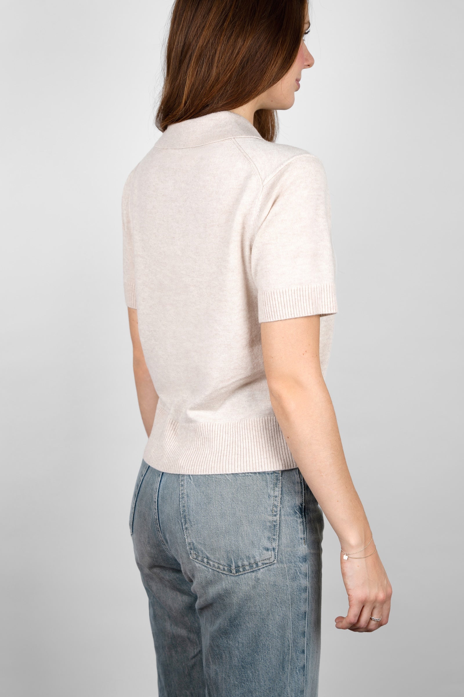 Angled back view of the CYME Short Sleeve Polo Shirt in beige, showing the collar, short sleeves and ribbed hem. Knitted in a soft, fine fabric for an easy, elevated fit.