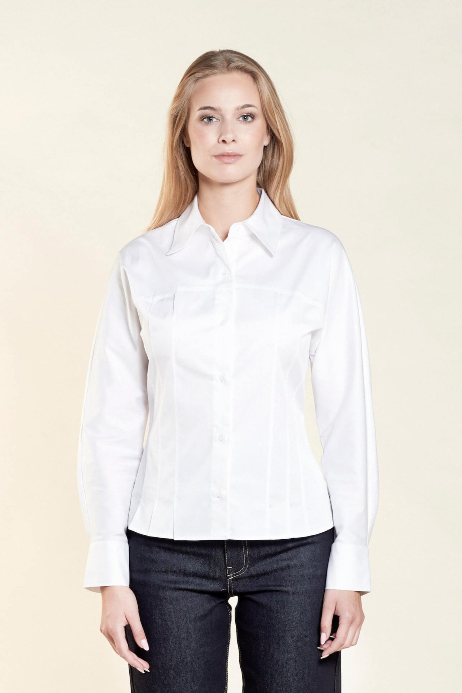 Front view of a woman with long blonde hair modeling a white button-down shirt paired with dark blue jeans from CYME Copenhagen. The image highlights the shirt's tailored fit and classic design, emphasizing the brand's commitment to high-quality, timeless fashion.