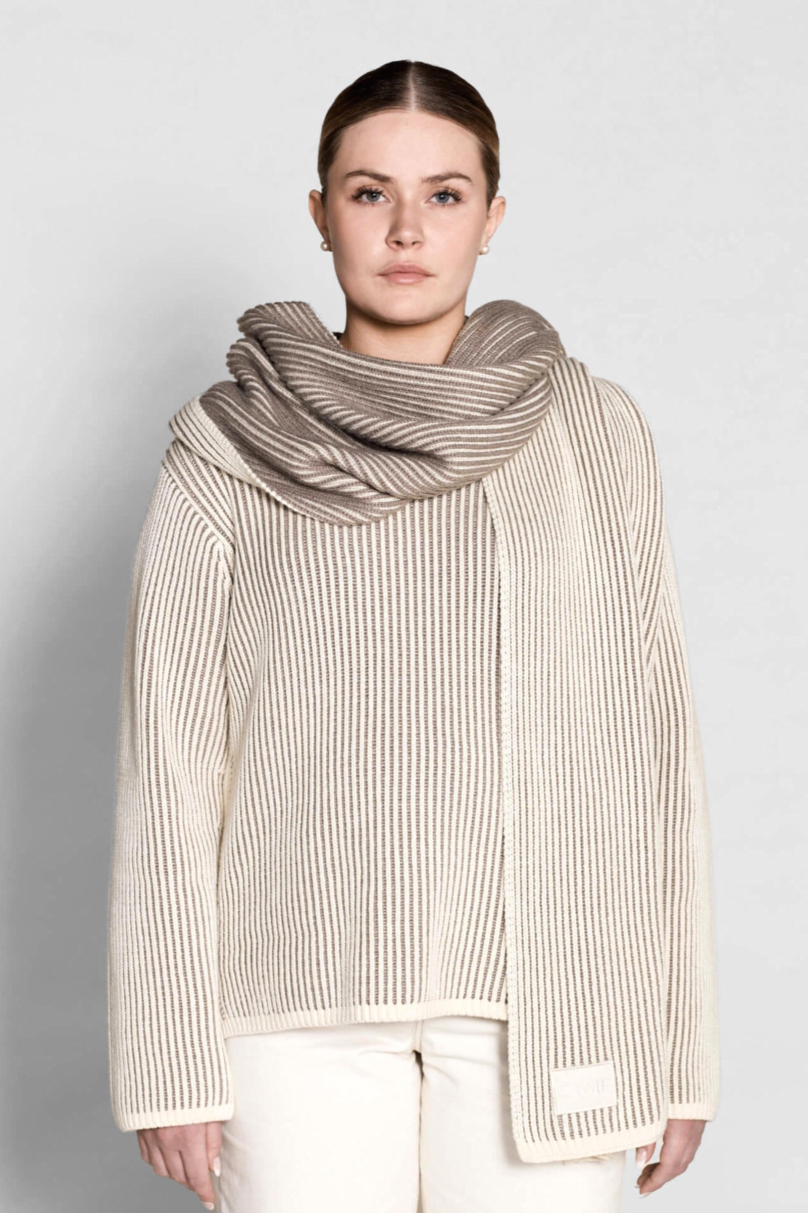 A model poses in Cyme Copenhagen's elegant cashmere knit sweater in cream, paired with a matching luxurious scarf, exemplifying the brand's commitment to sustainable fashion and natural materials.