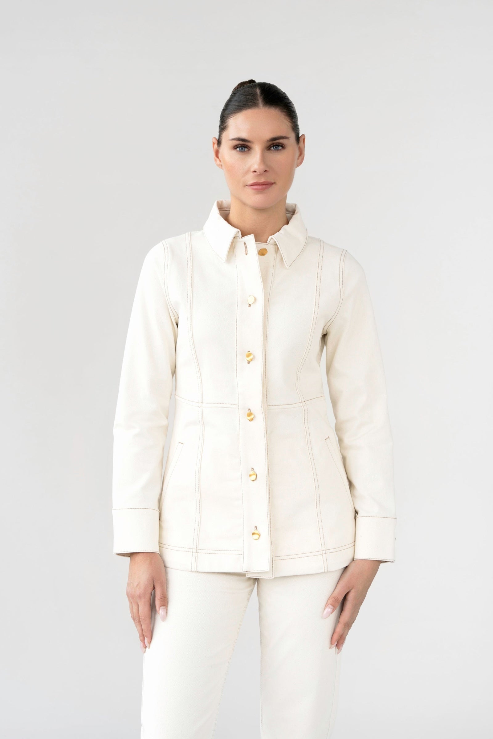 Woman wearing a white jacket with gold buttons on a plain background