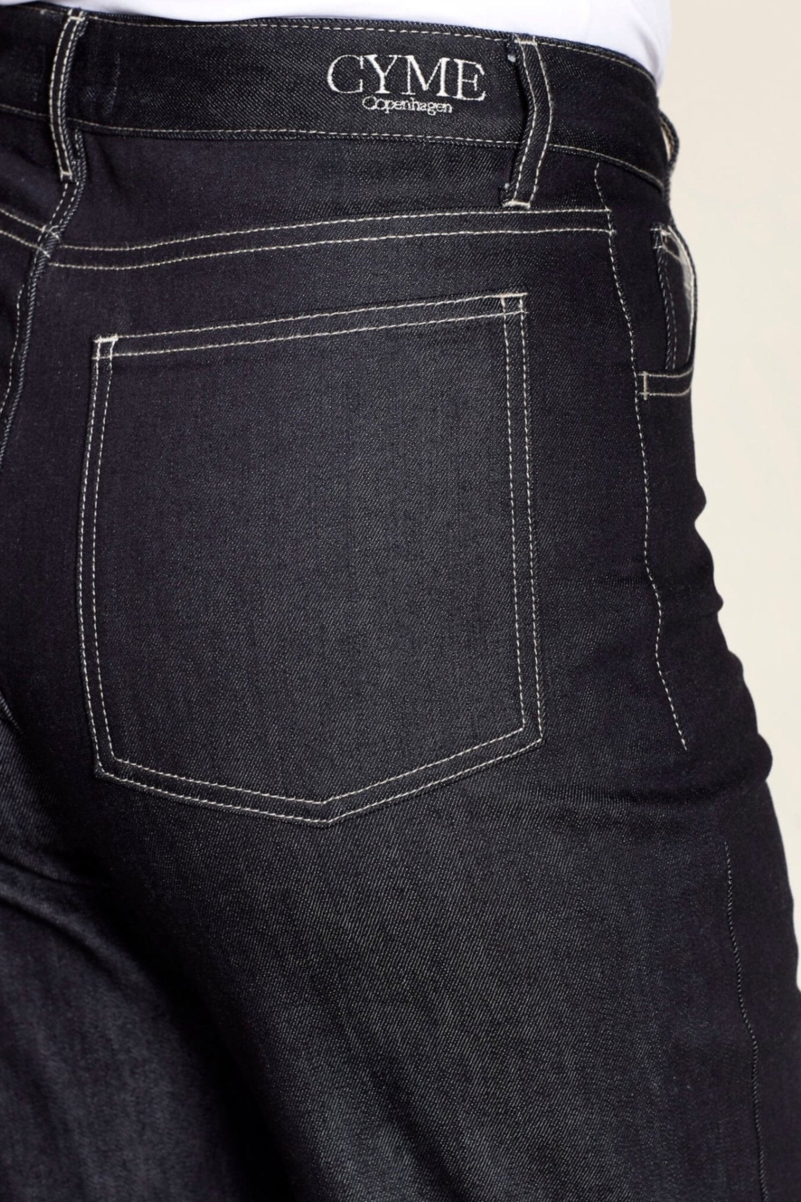 Detail of Cyme Copenhagen's premium denim jeans featuring contrast stitching and the brand's logo, exemplifying the luxury and craftsmanship of Danish designer clothing.