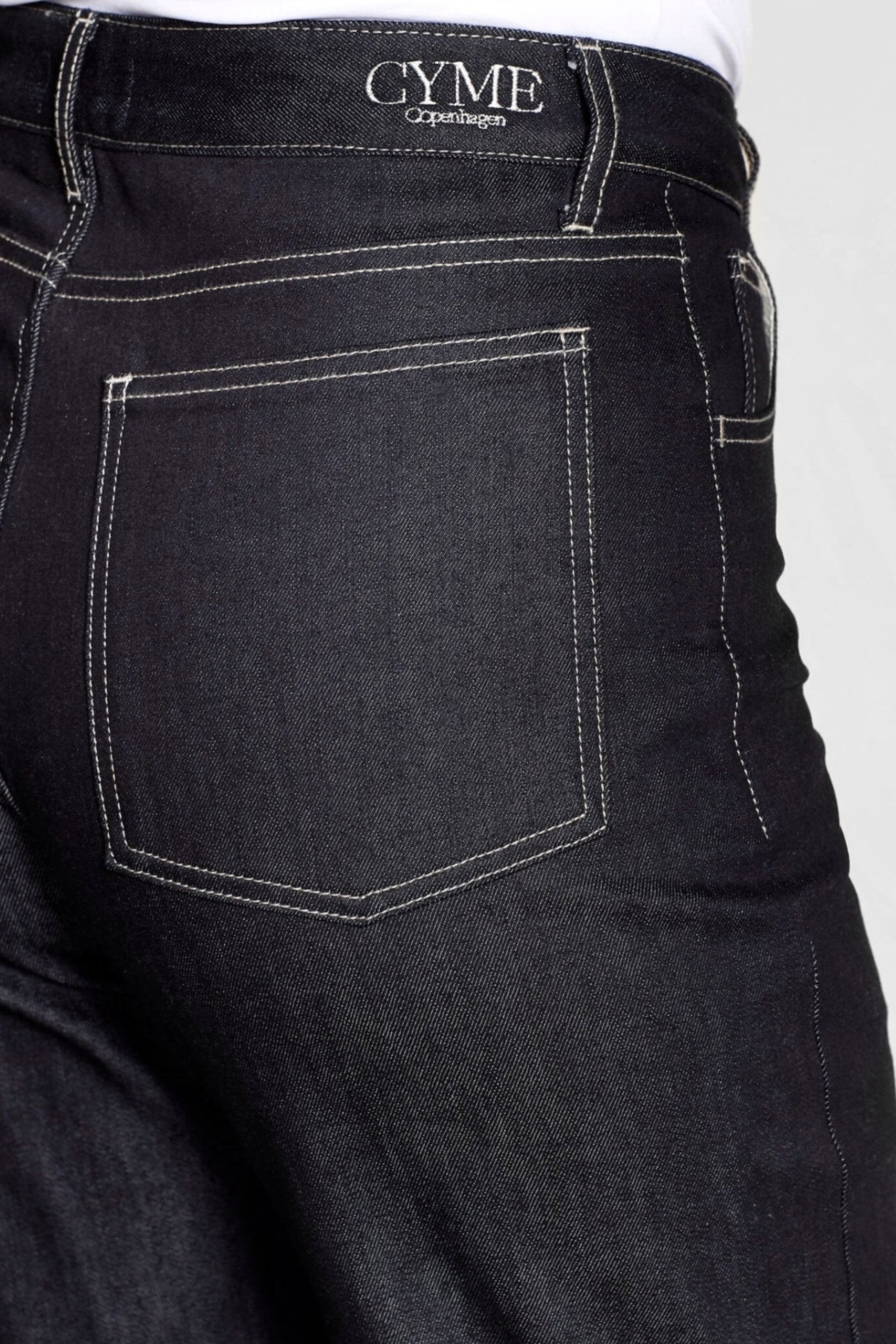 Detail of Cyme Copenhagen's premium denim jeans featuring contrast stitching and the brand's logo, exemplifying the luxury and craftsmanship of Danish designer clothing.