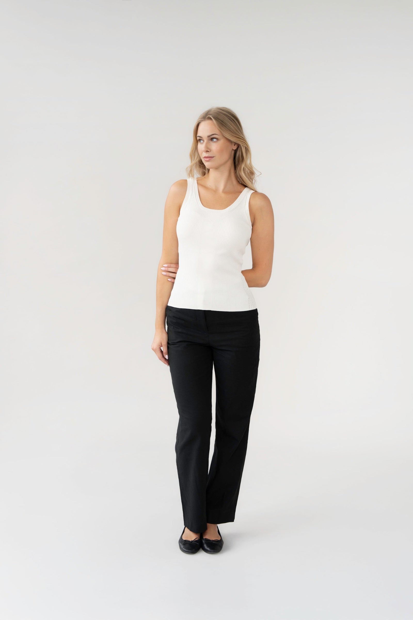 Woman wearing a white sleeveless top and black pants on a white background