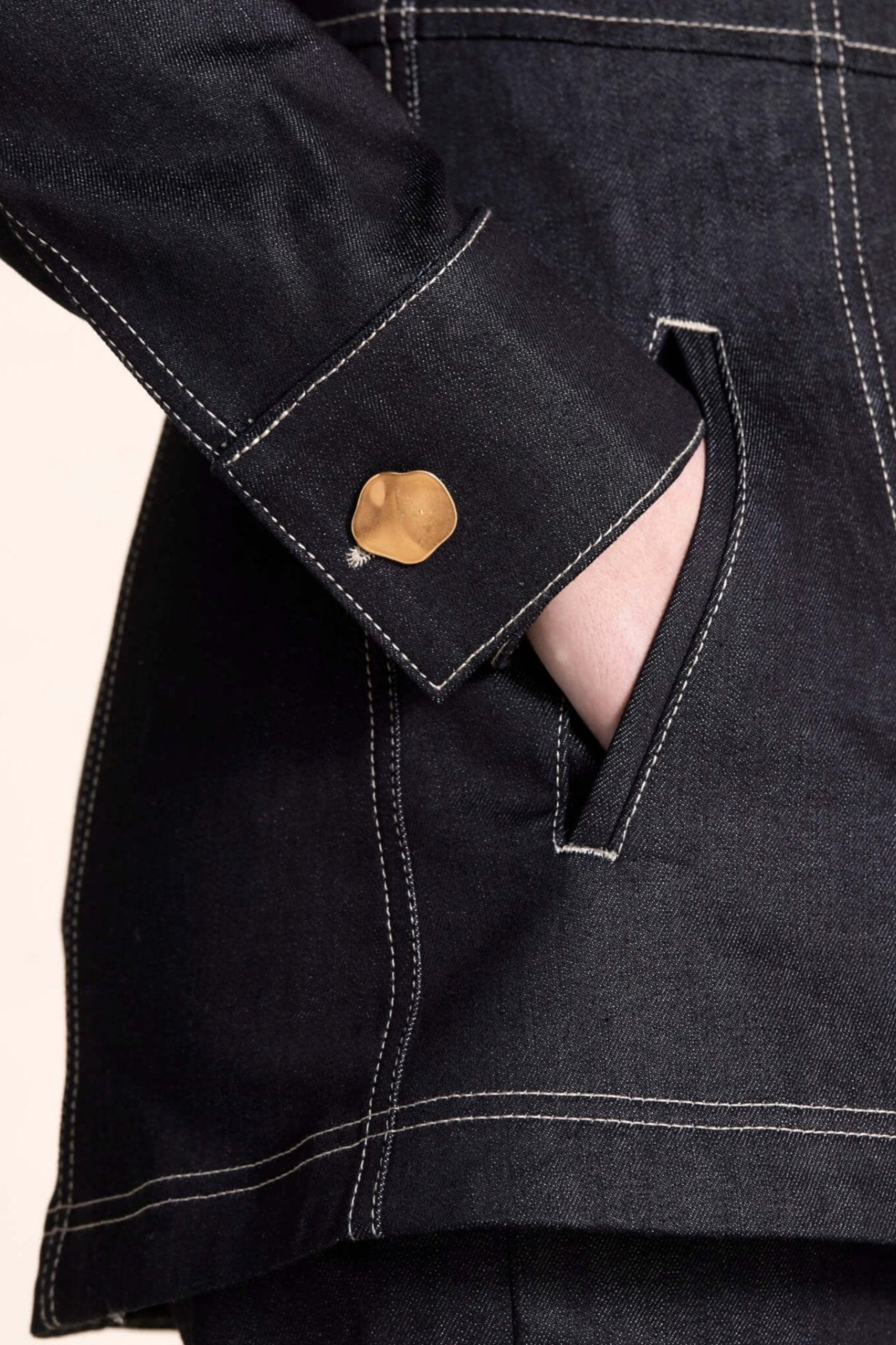 Close-up on the detail of a Cyme Copenhagen denim jacket with golden button cuff, showcasing the brand's attention to detail and dedication to ethical fashion with a Scandinavian touch.