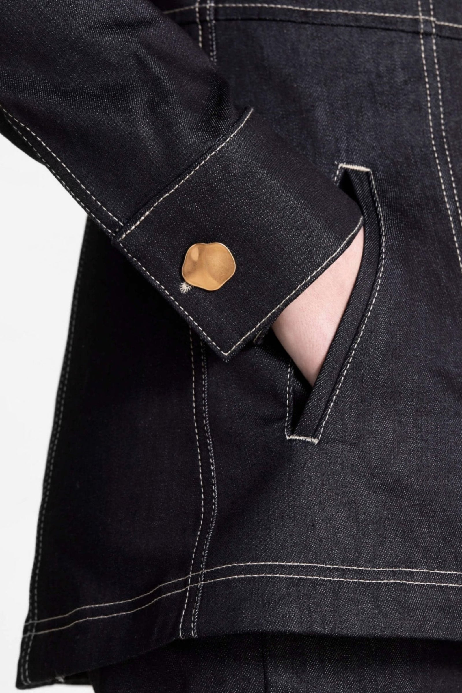 Close-up on the detail of a Cyme Copenhagen denim jacket with golden button cuff, showcasing the brand's attention to detail and dedication to ethical fashion with a Scandinavian touch.
