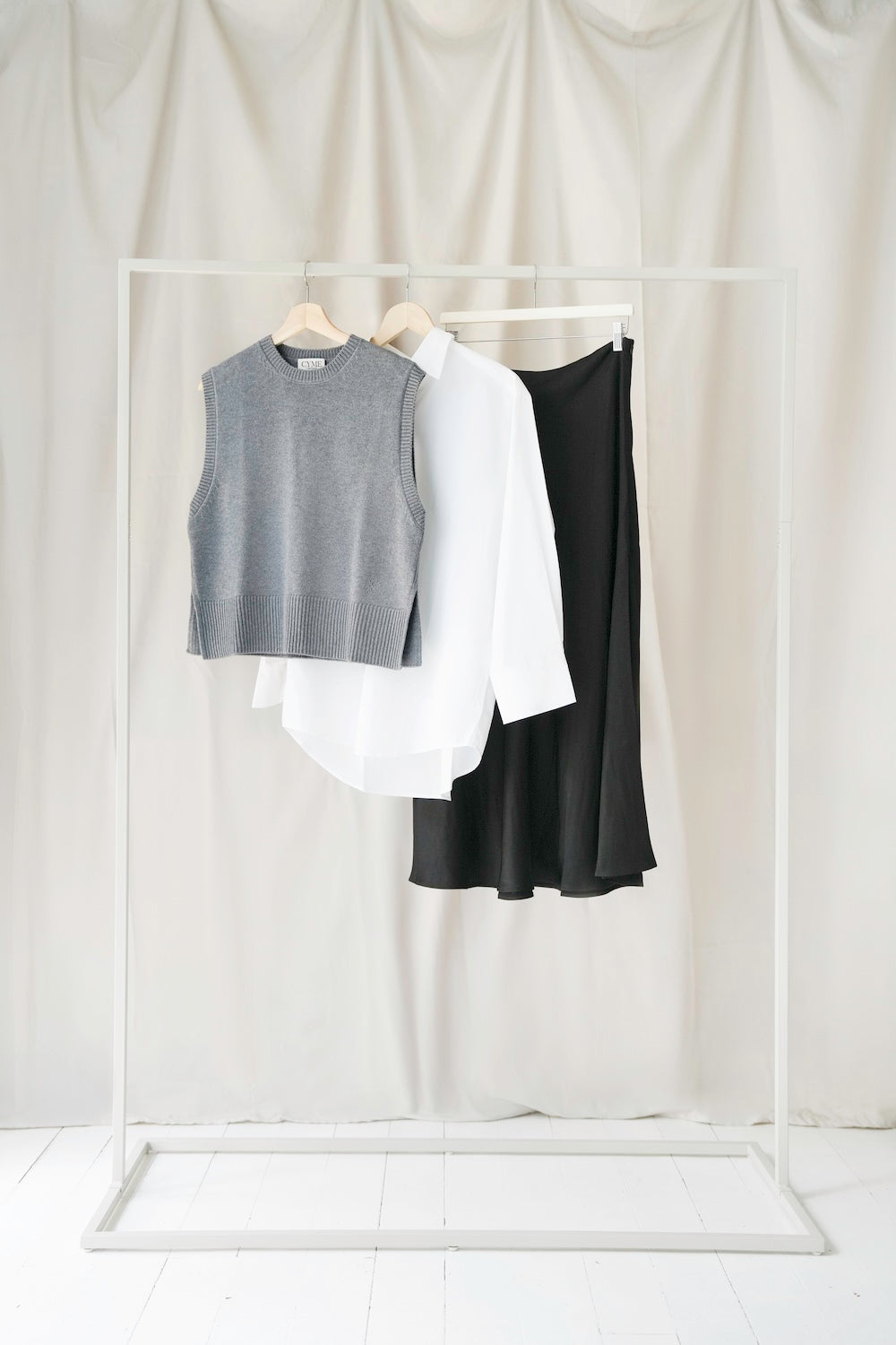 CYME grey merino vest, white Supima shirt and black satin skirt arranged on a clothing rack.