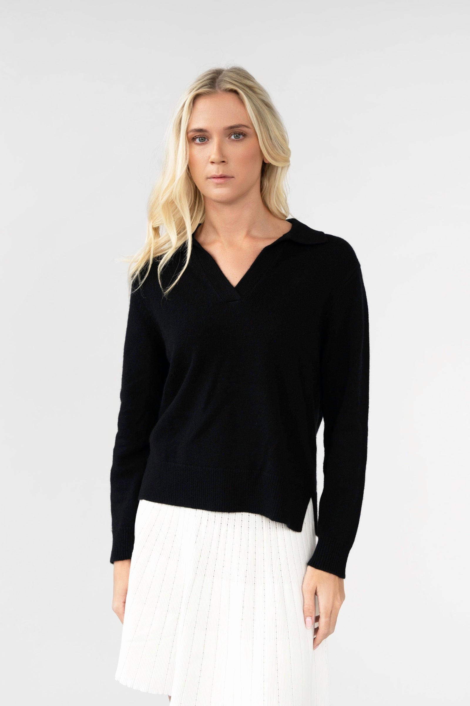 Woman wearing a black sweater and white pleated skirt on a plain background