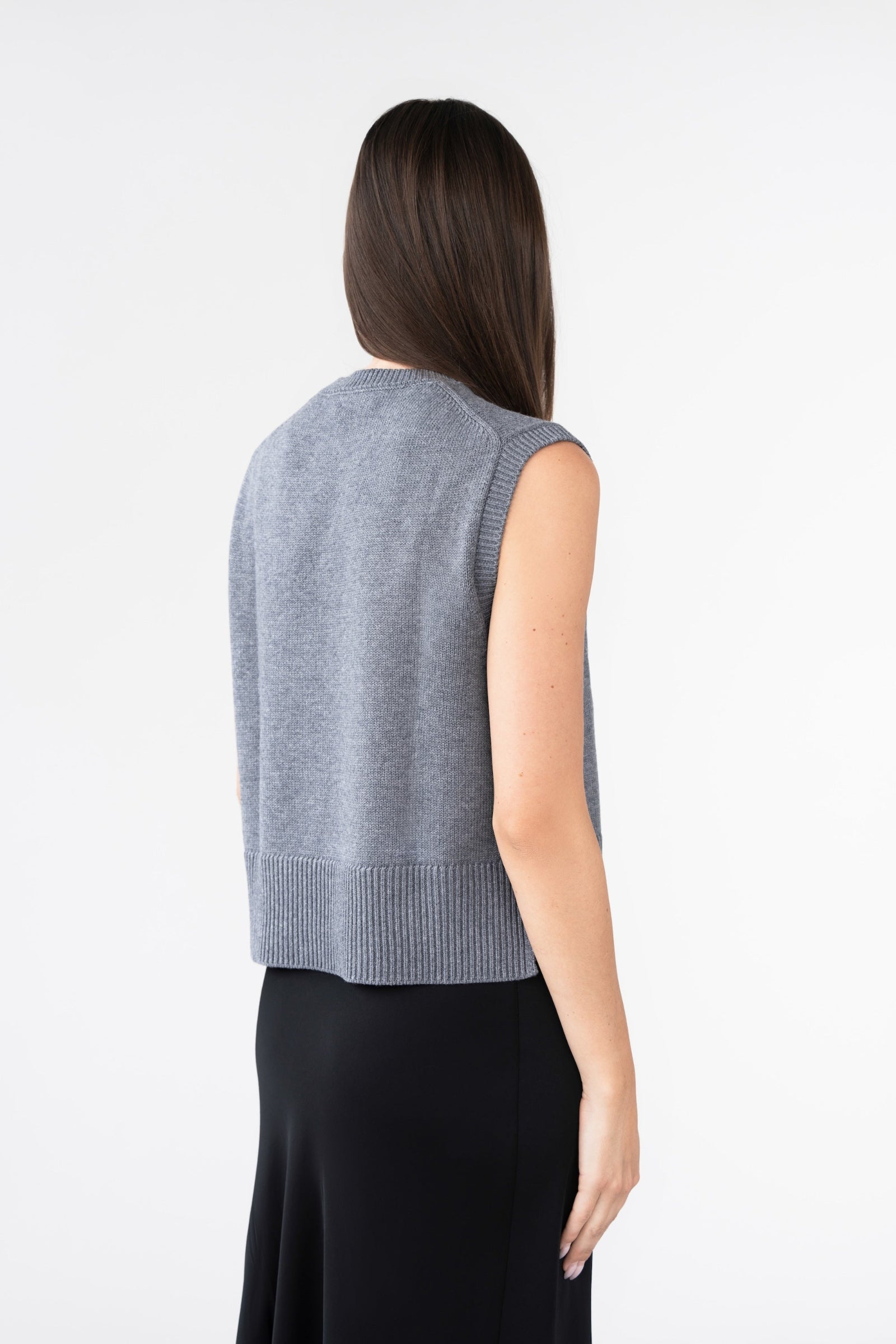 A woman wearing a grey knitted vest standing facing away.