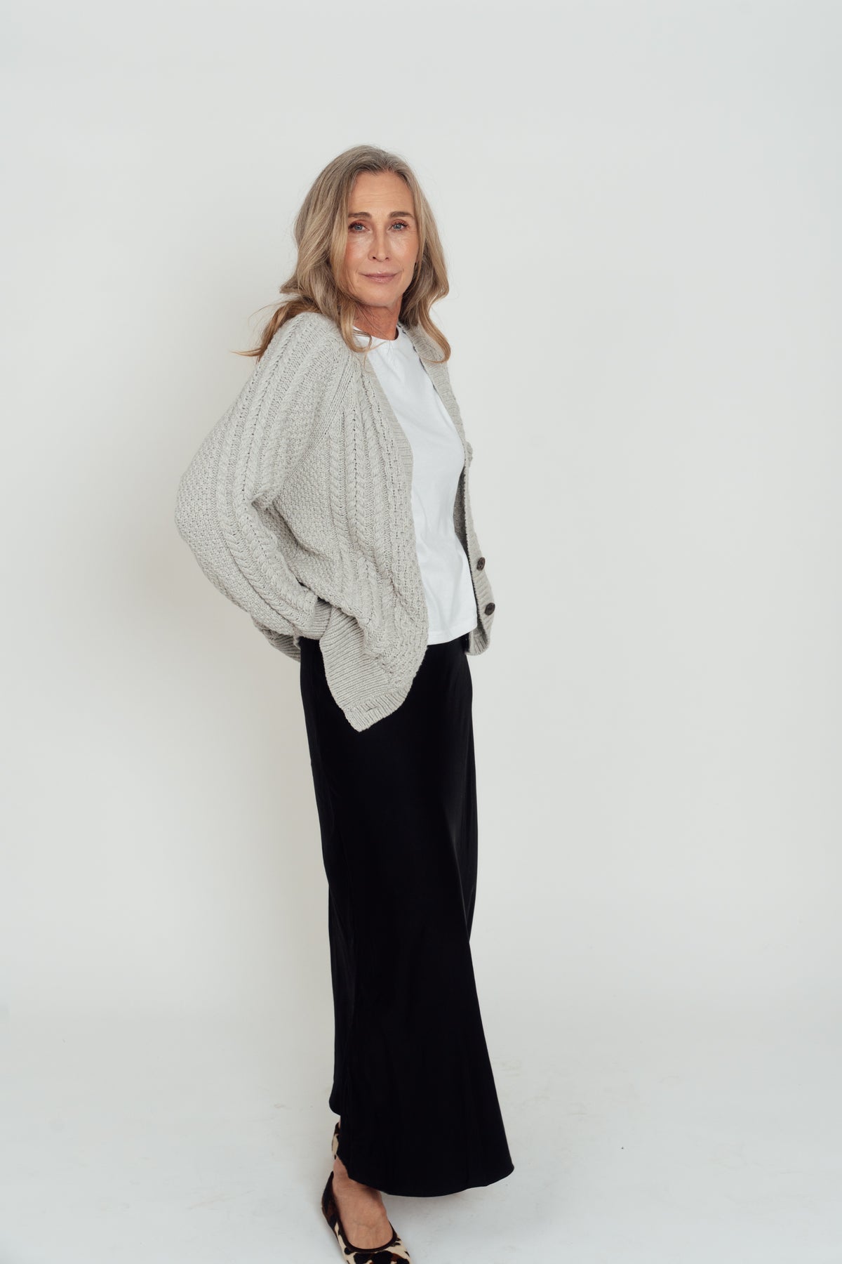 Angled view of the grey Hazel Cable Knit Cardigan worn open, showing the cable-knit sleeve and ribbed hem.